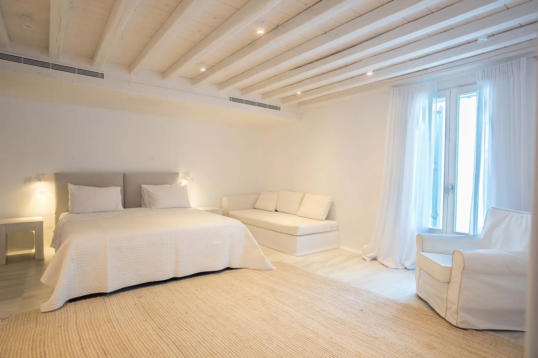 A bright bedroom with a bed, a small sofa, and an armchair.