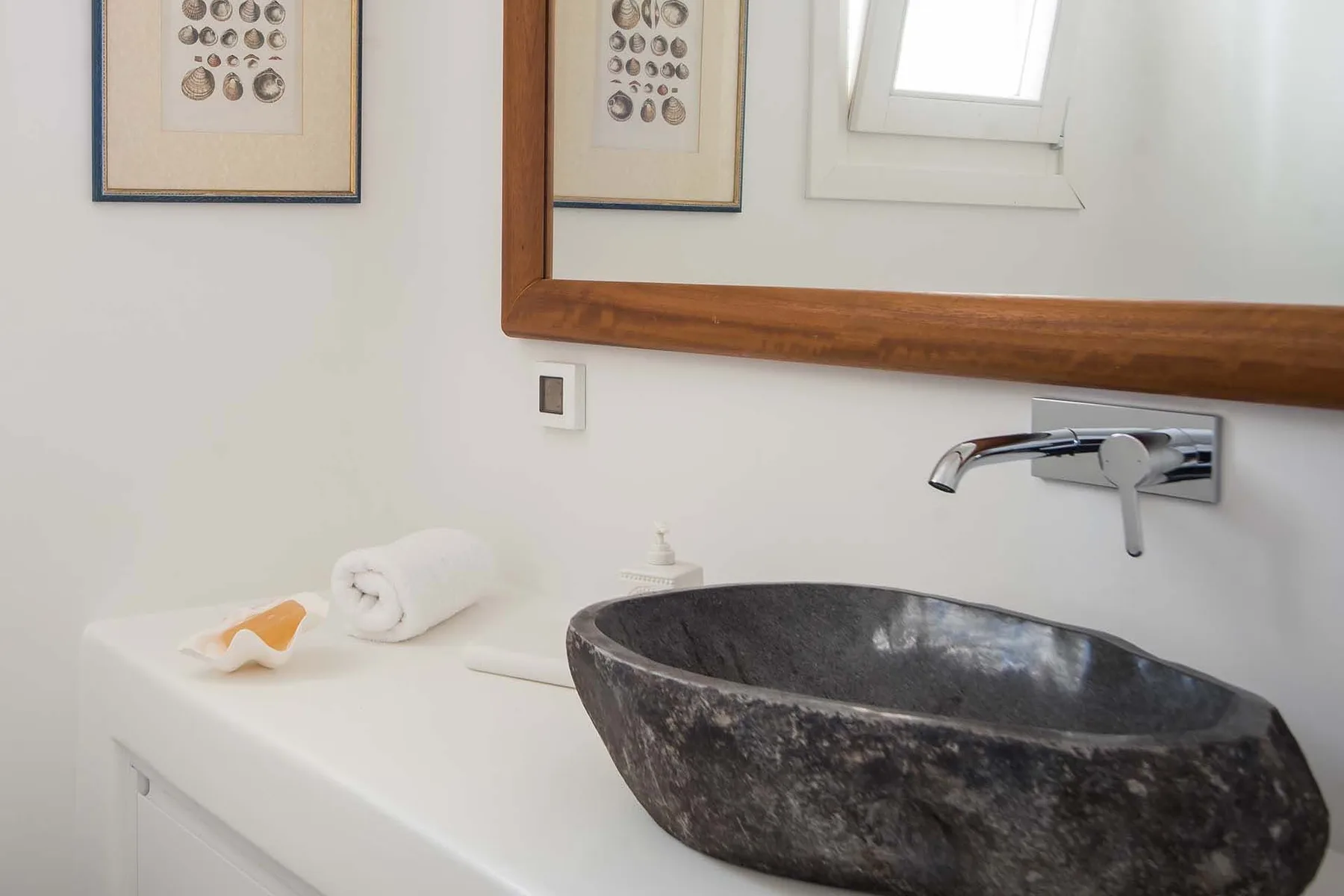 A bathroom vanity with a dark stone vessel sink and wall-mounted faucet.