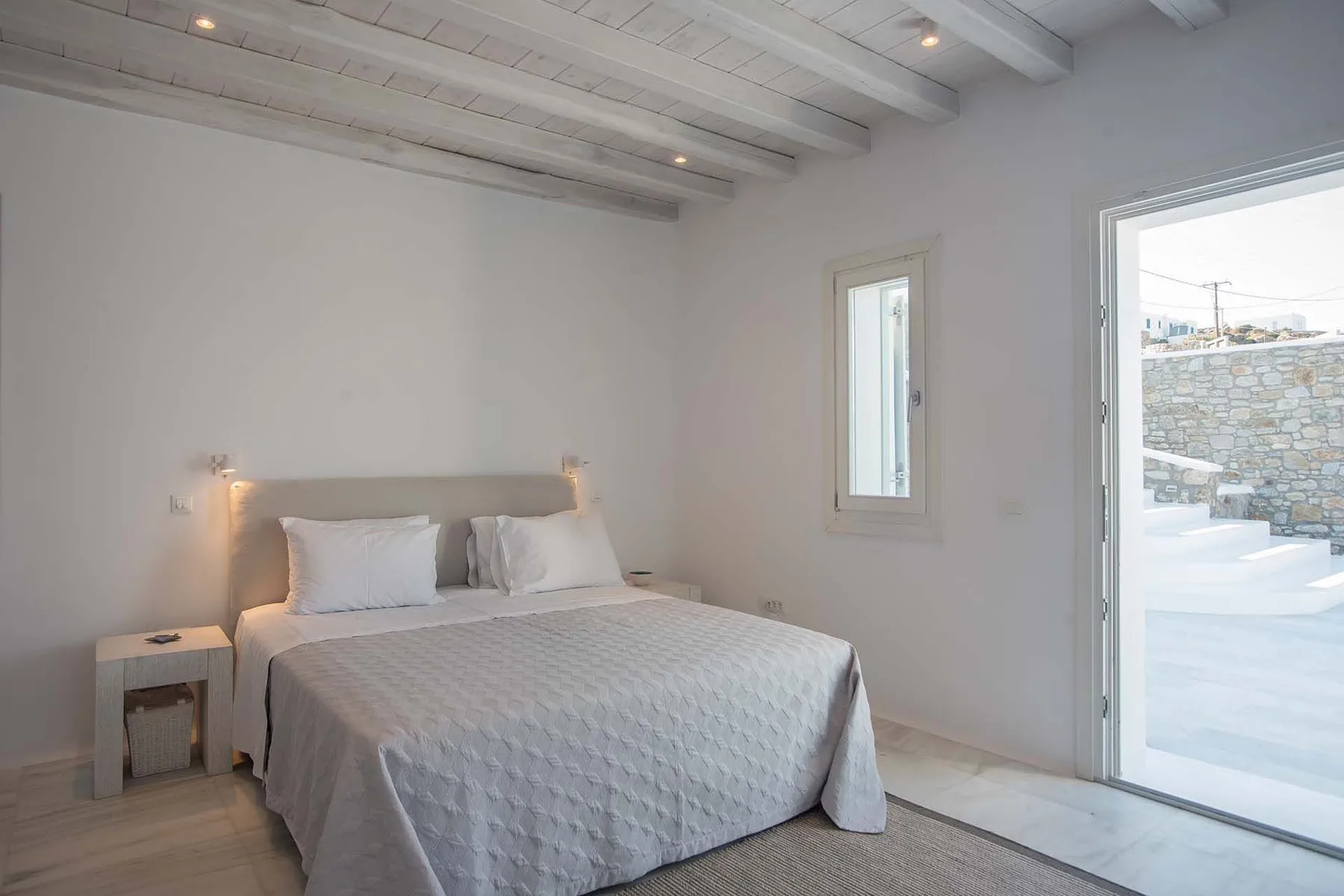 A bright bedroom with a neatly made bed beside an open glass door.