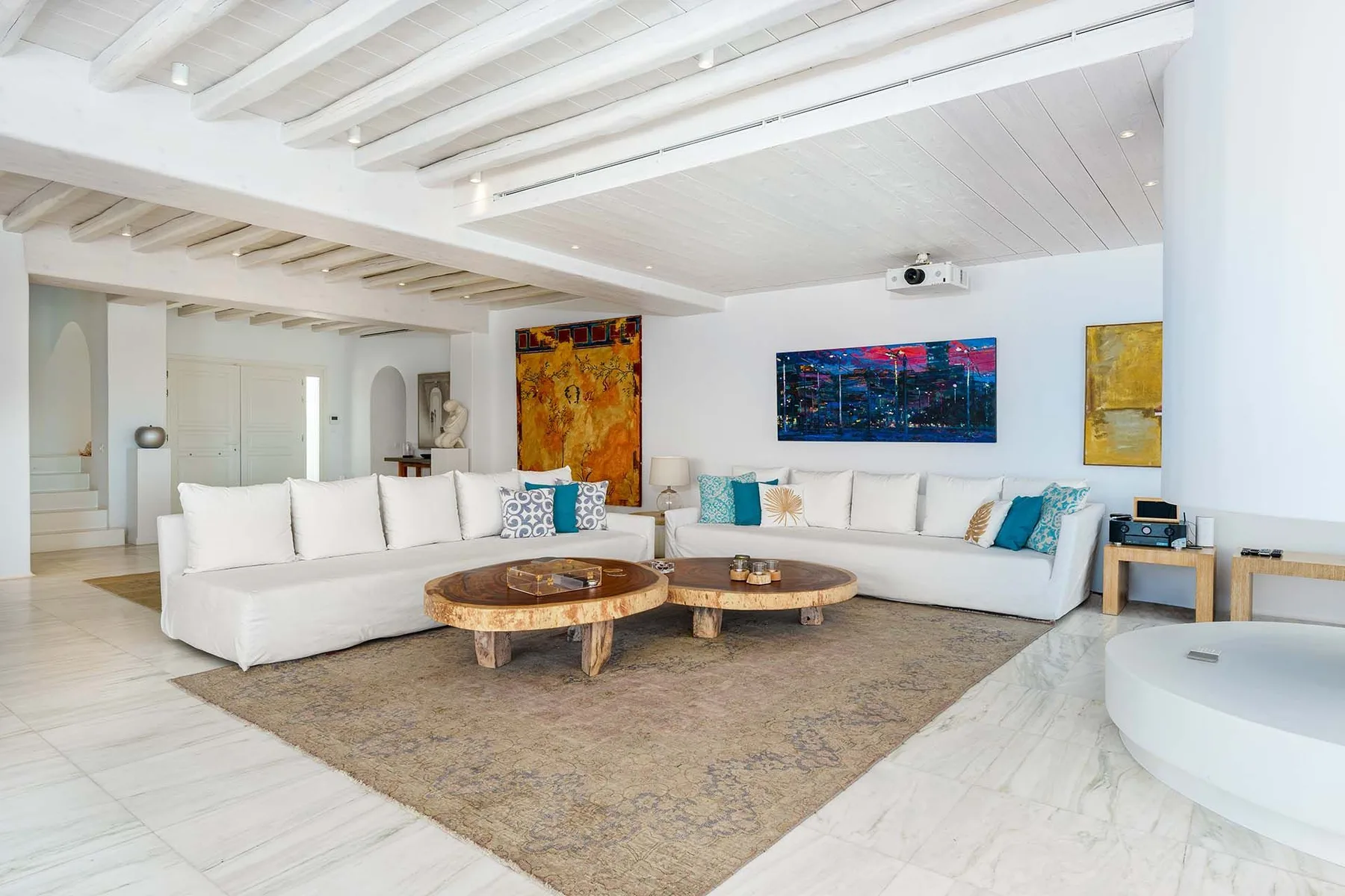A bright living room with white seating arranged around low wooden tables.