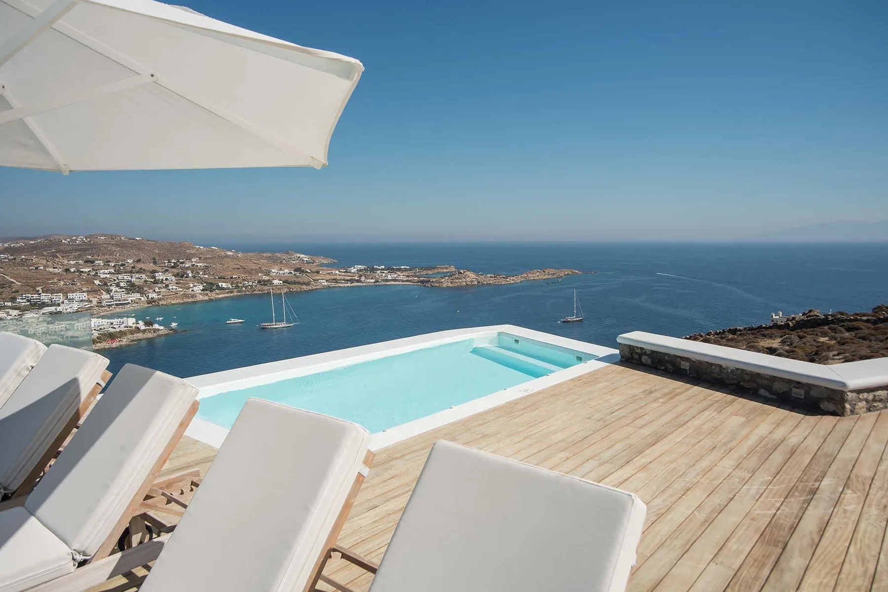 A rooftop pool and deck overlook the sea and a coastal town.