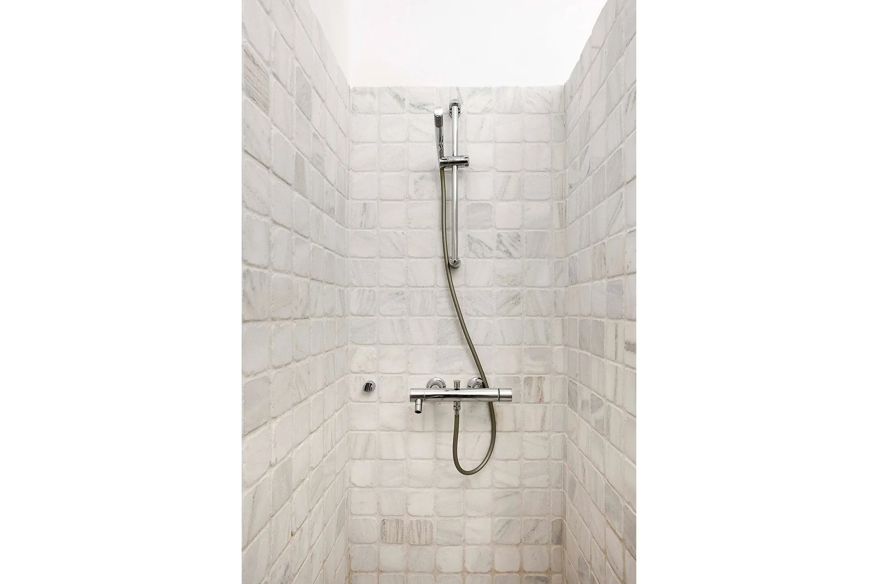 A tiled shower with a wall-mounted showerhead and control bar.