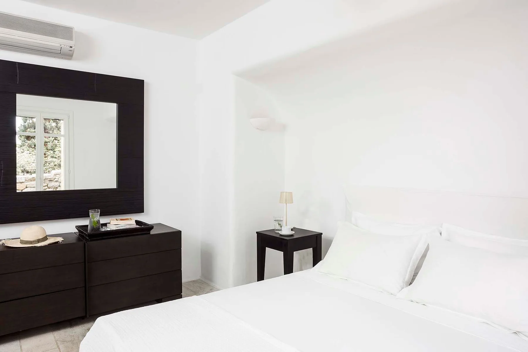 A bright bedroom with a neatly made bed and a dark dresser beneath a large mirror.