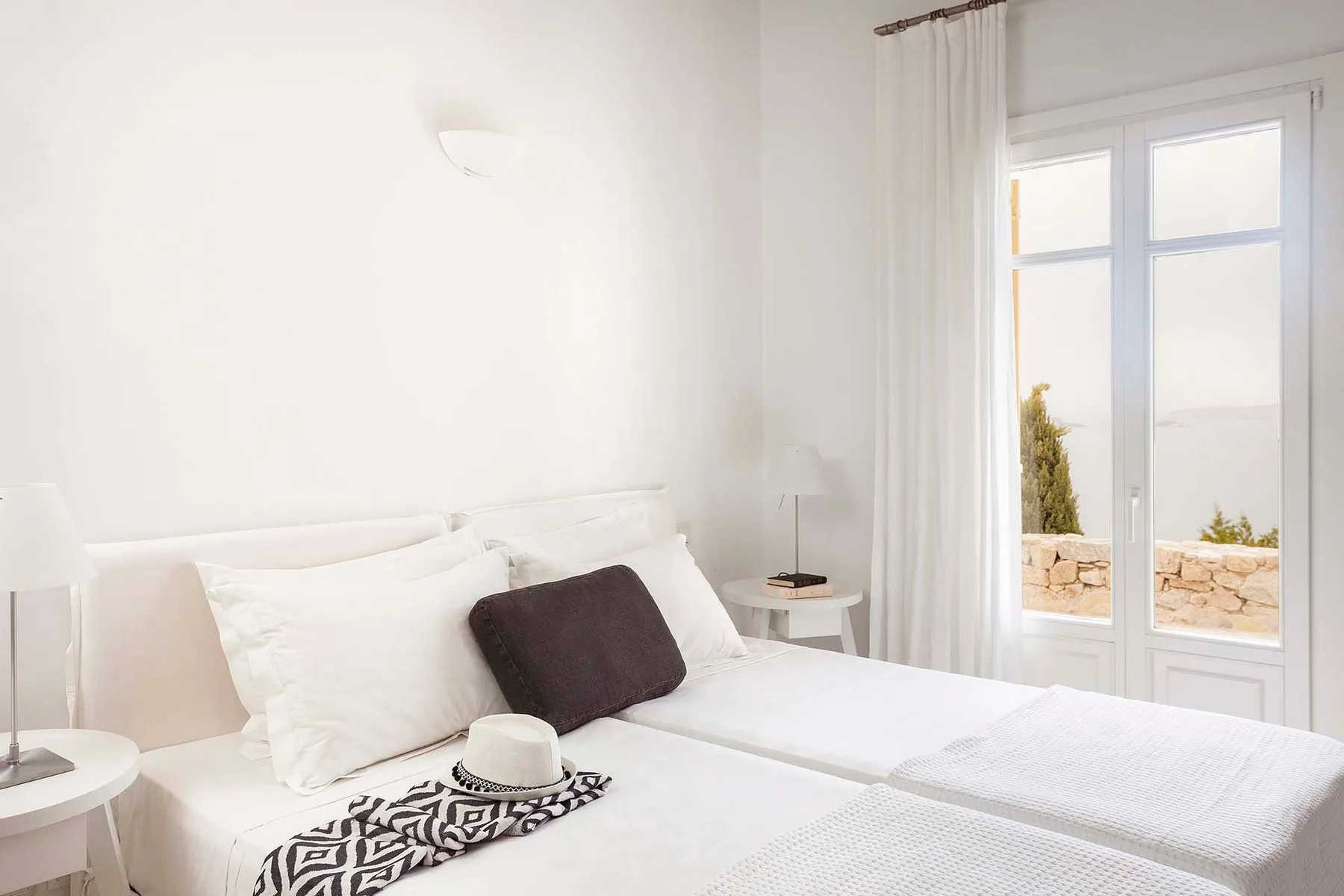 A bright bedroom with white bedding and a tall window.