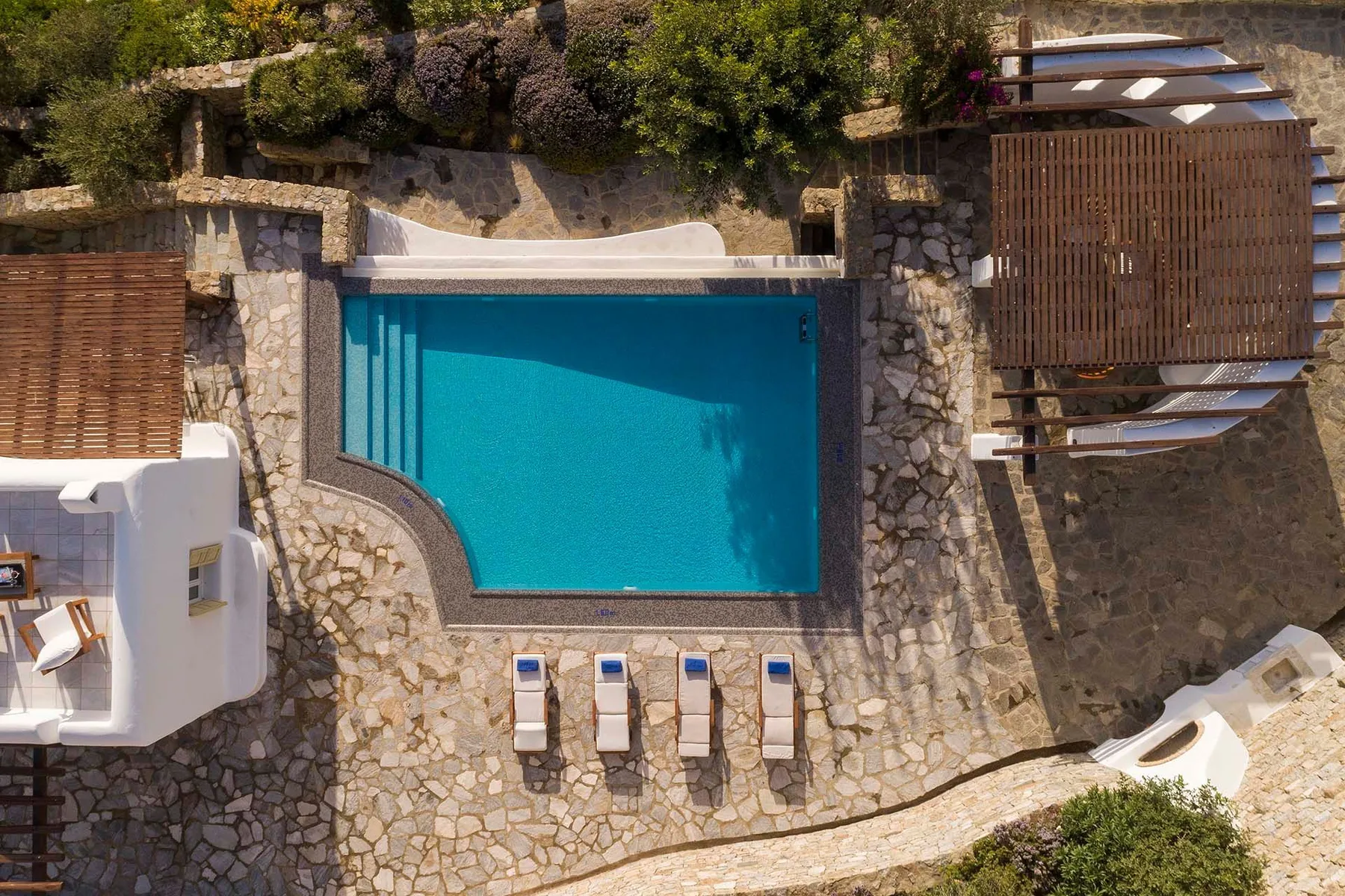 An outdoor swimming pool is surrounded by stone paving and seating.