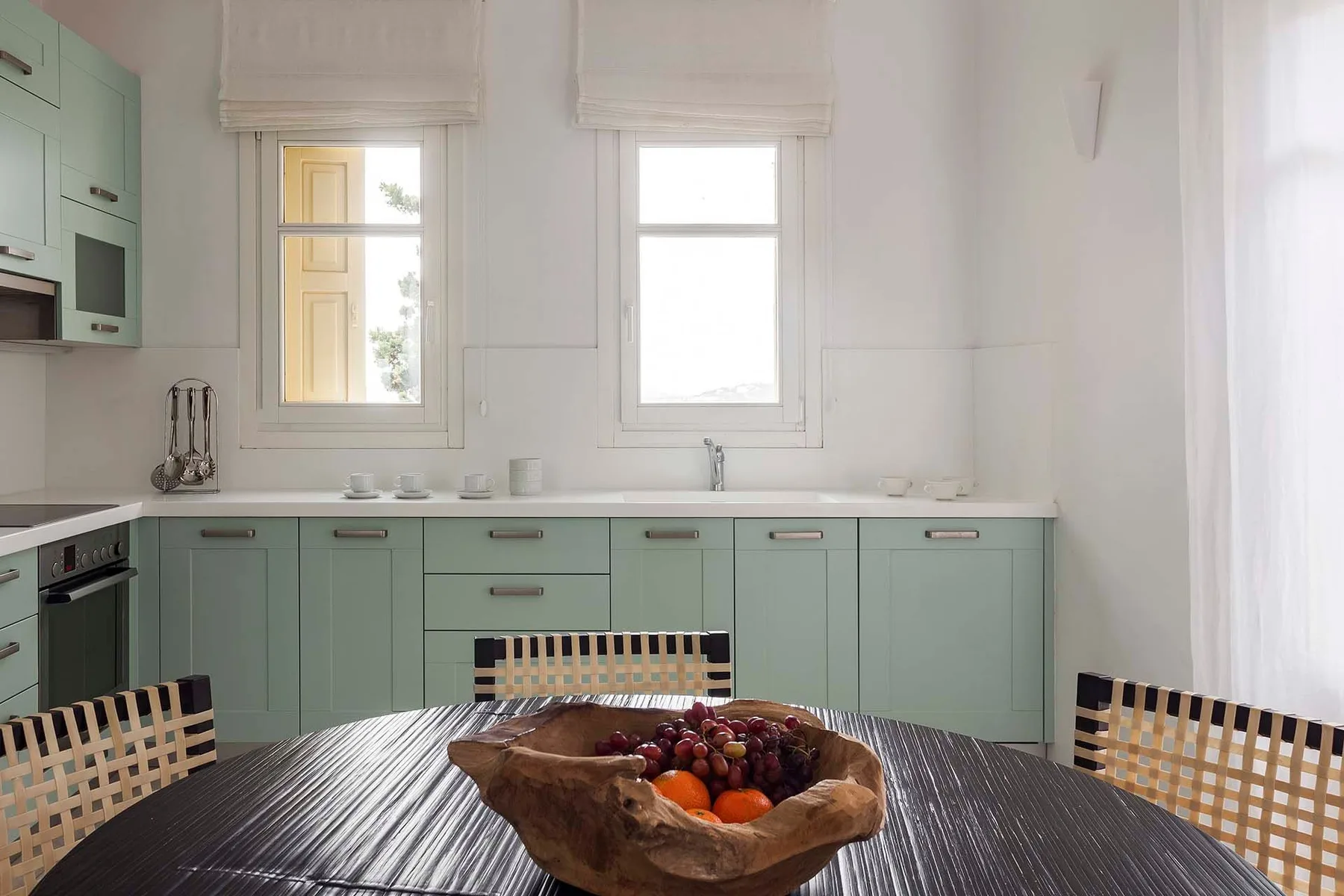A bright kitchen with pale green cabinets and a round dining table.
