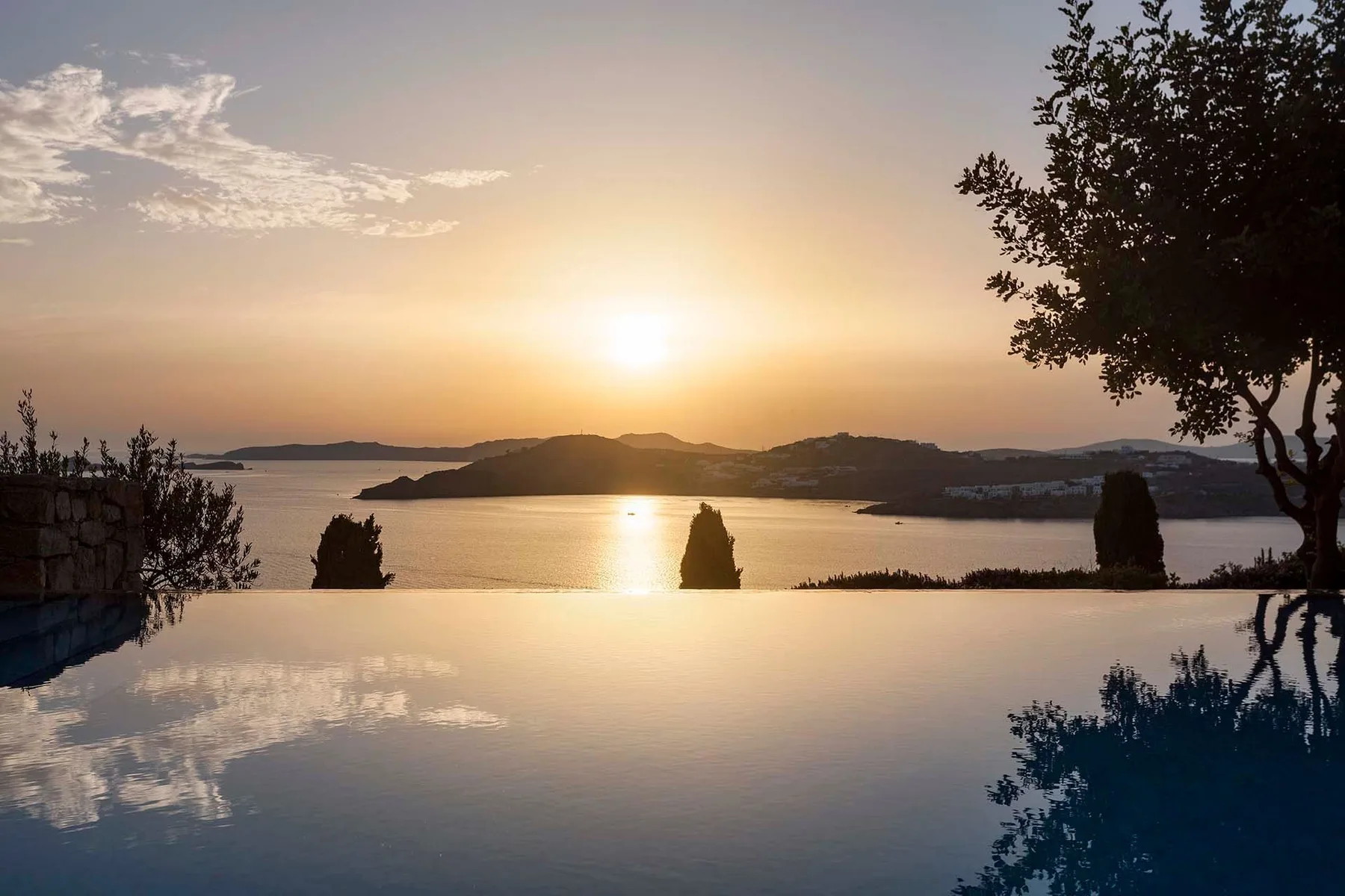 A sunset over calm water is reflected in an infinity pool.