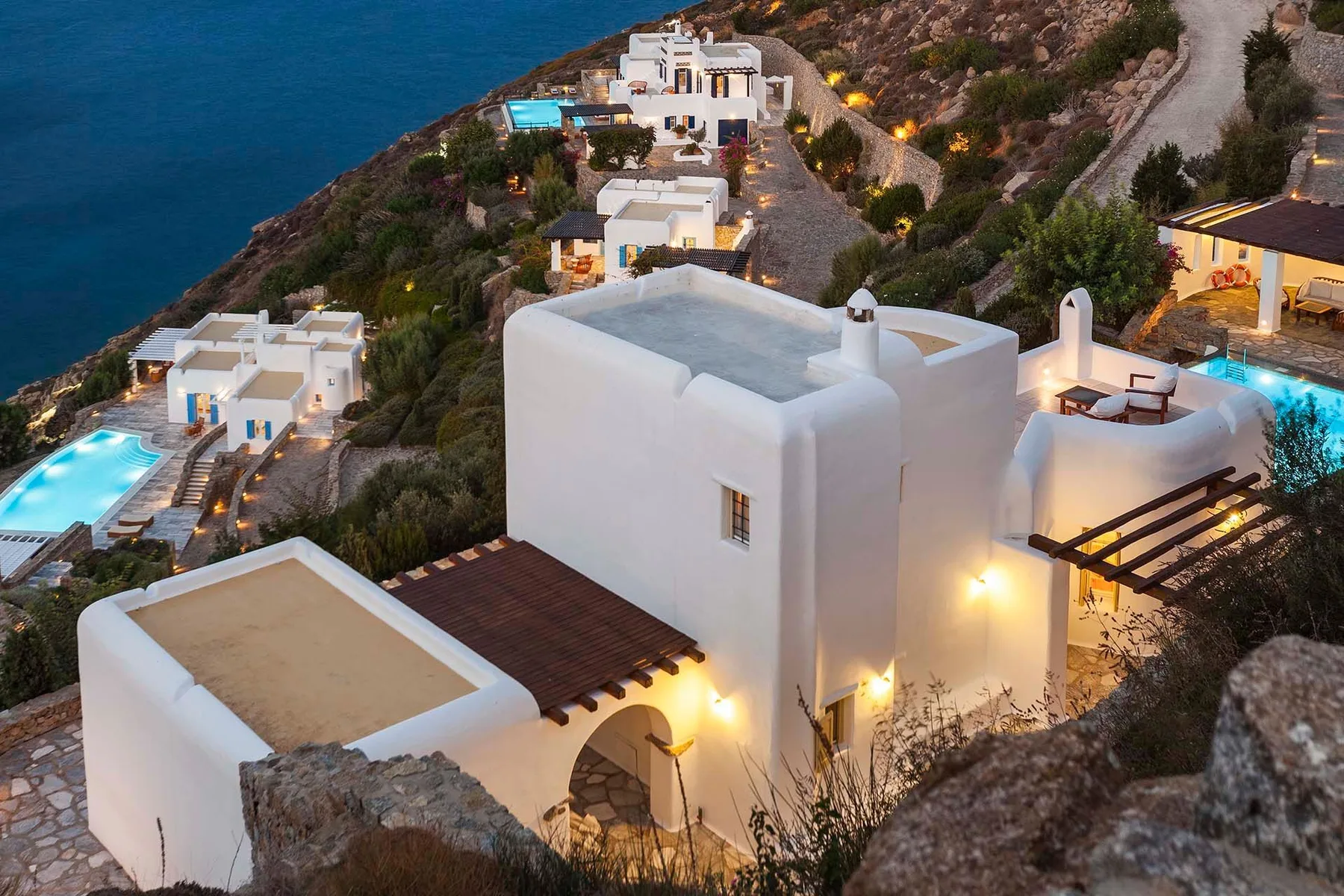 White buildings and illuminated pools dot a hillside above the sea.