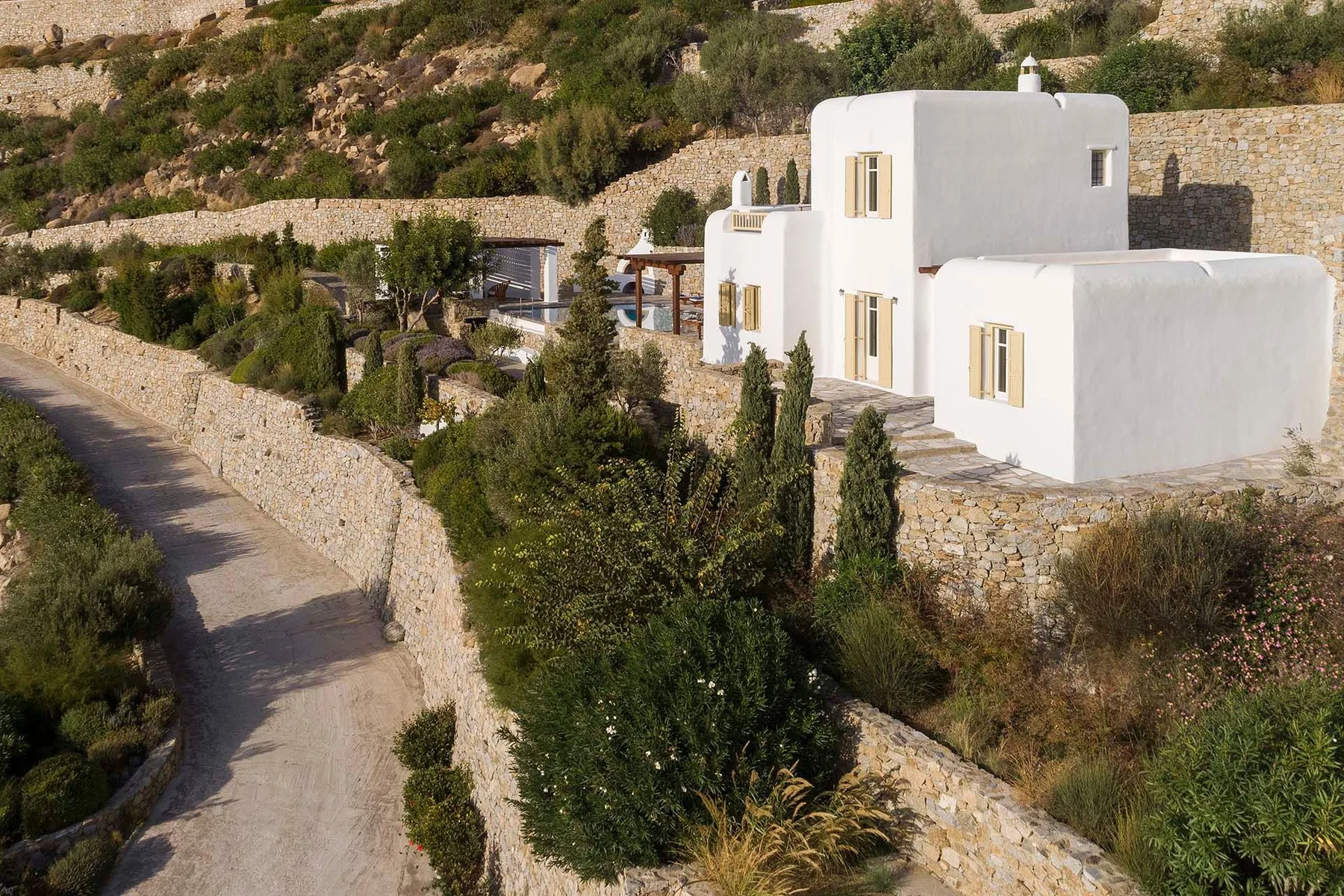 White buildings sit among stone walls and greenery beside a winding road.