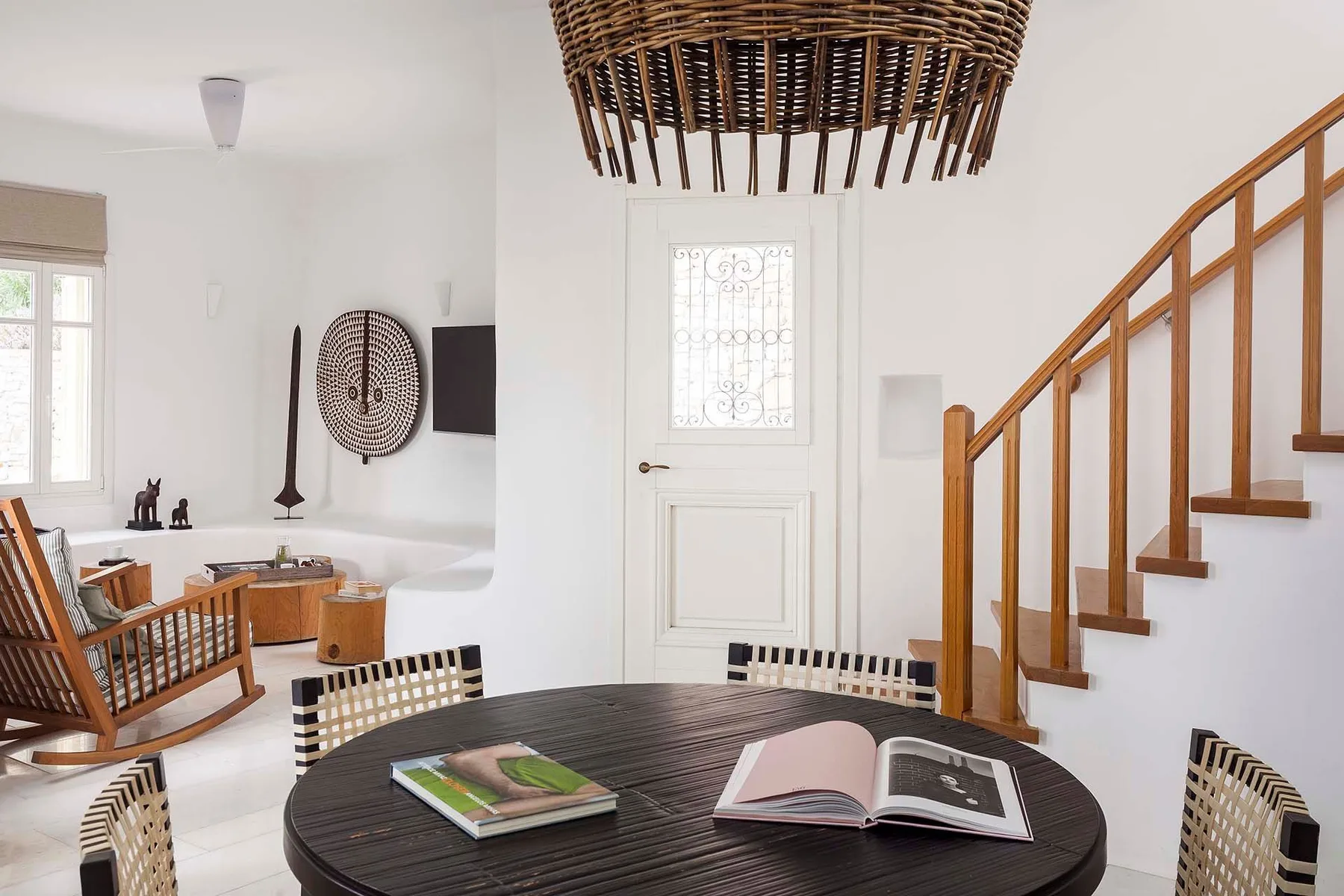 A bright living area with a round table, woven seating, and a staircase.