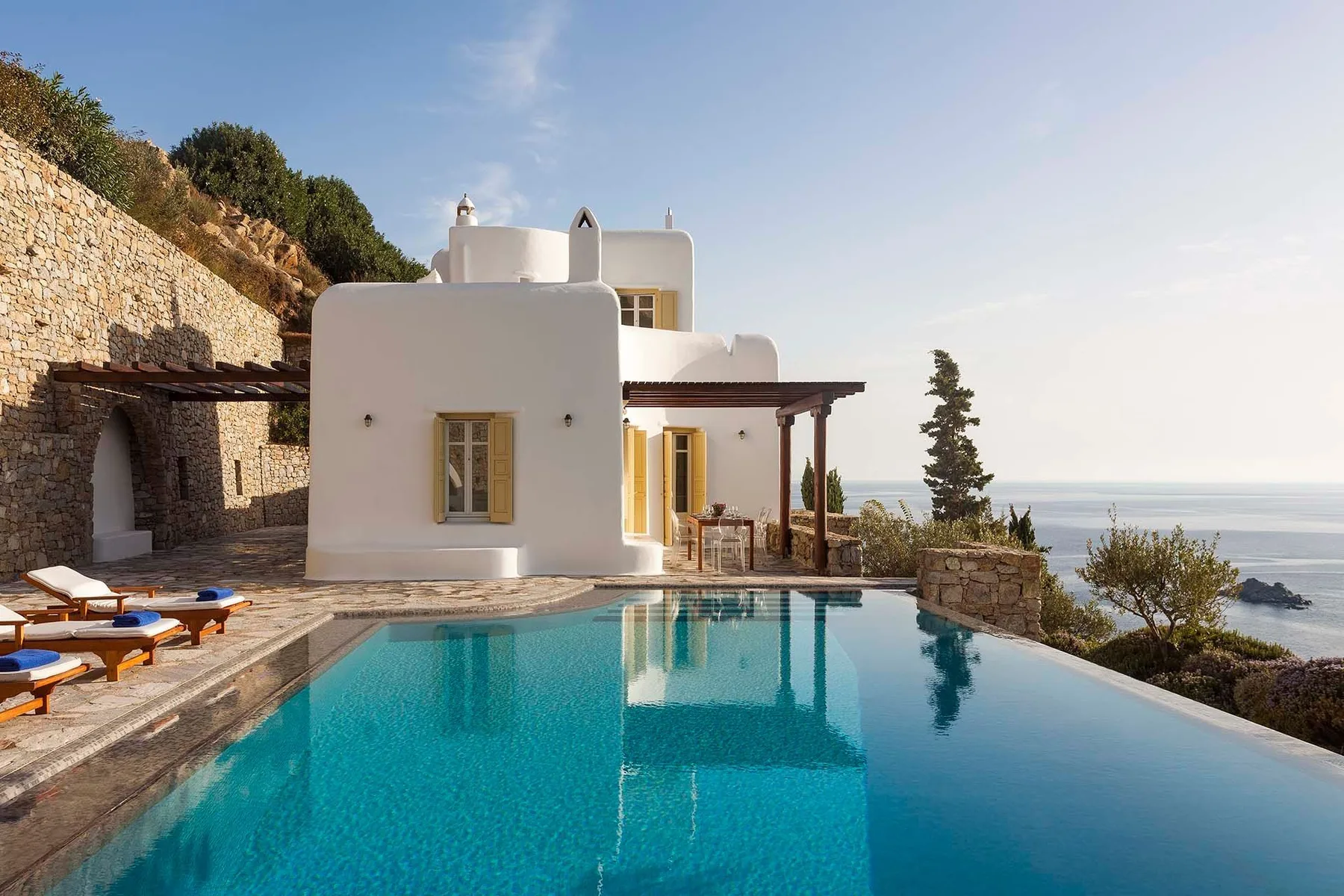 A white house beside a swimming pool overlooking the sea.