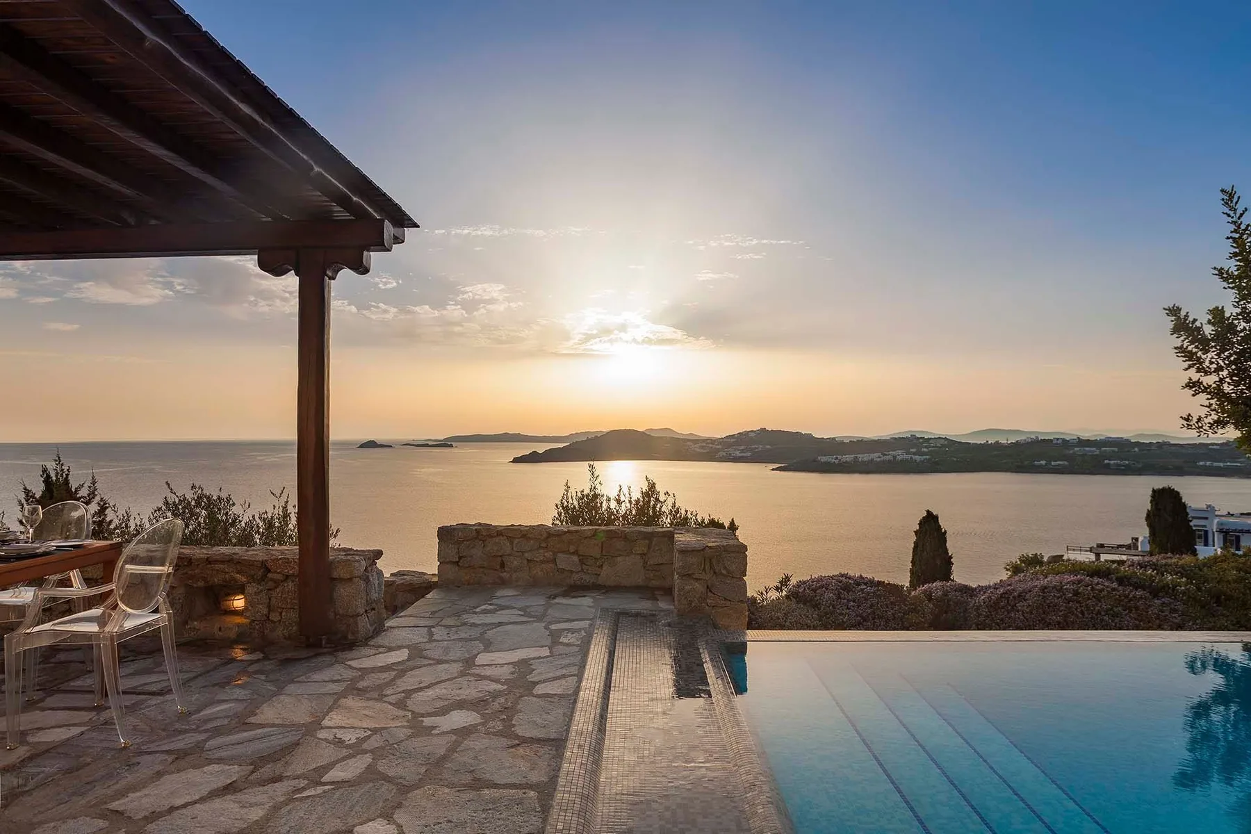 A stone terrace and swimming pool overlook the sea at sunset.