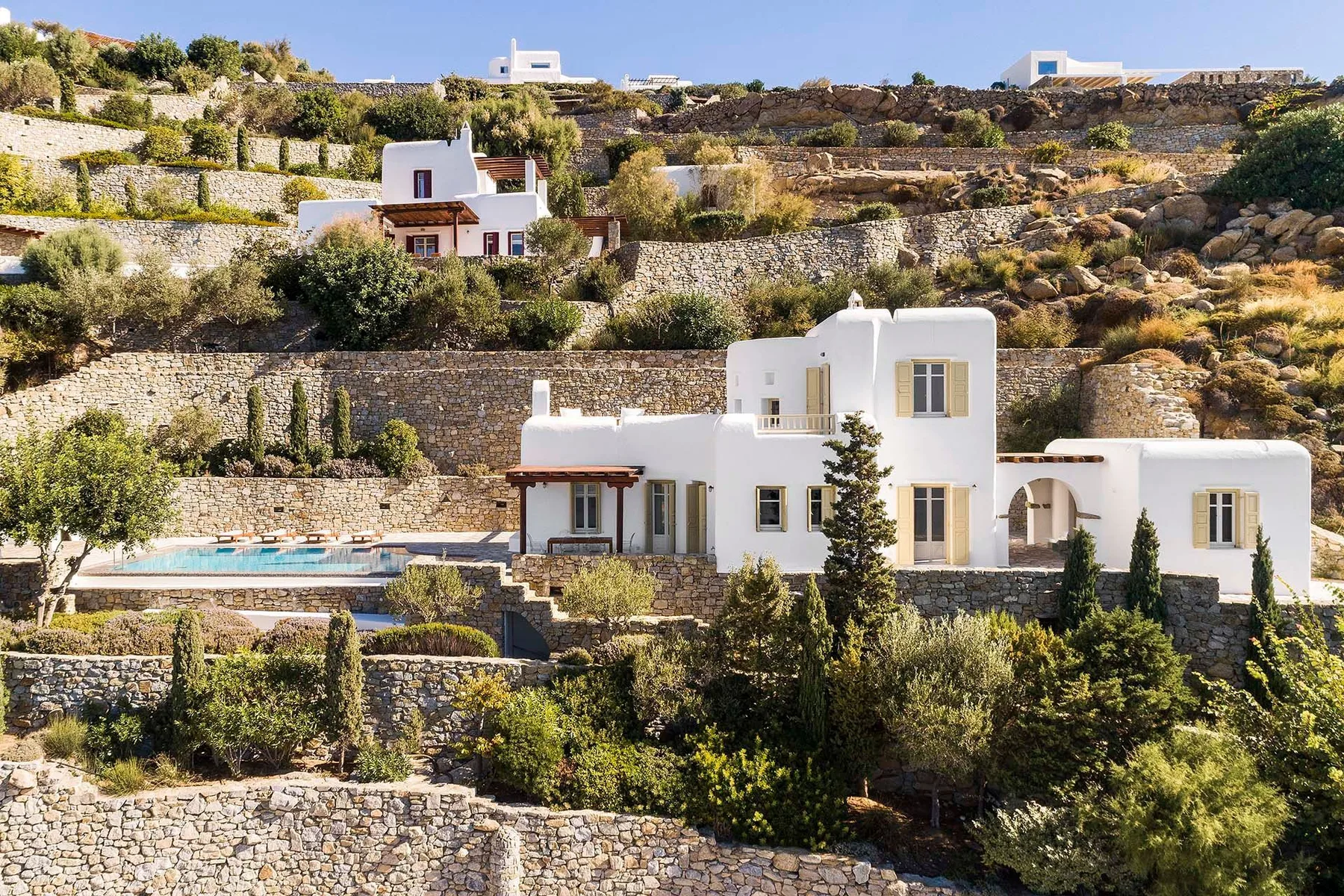 White houses sit among terraced stone walls and greenery on a hillside.