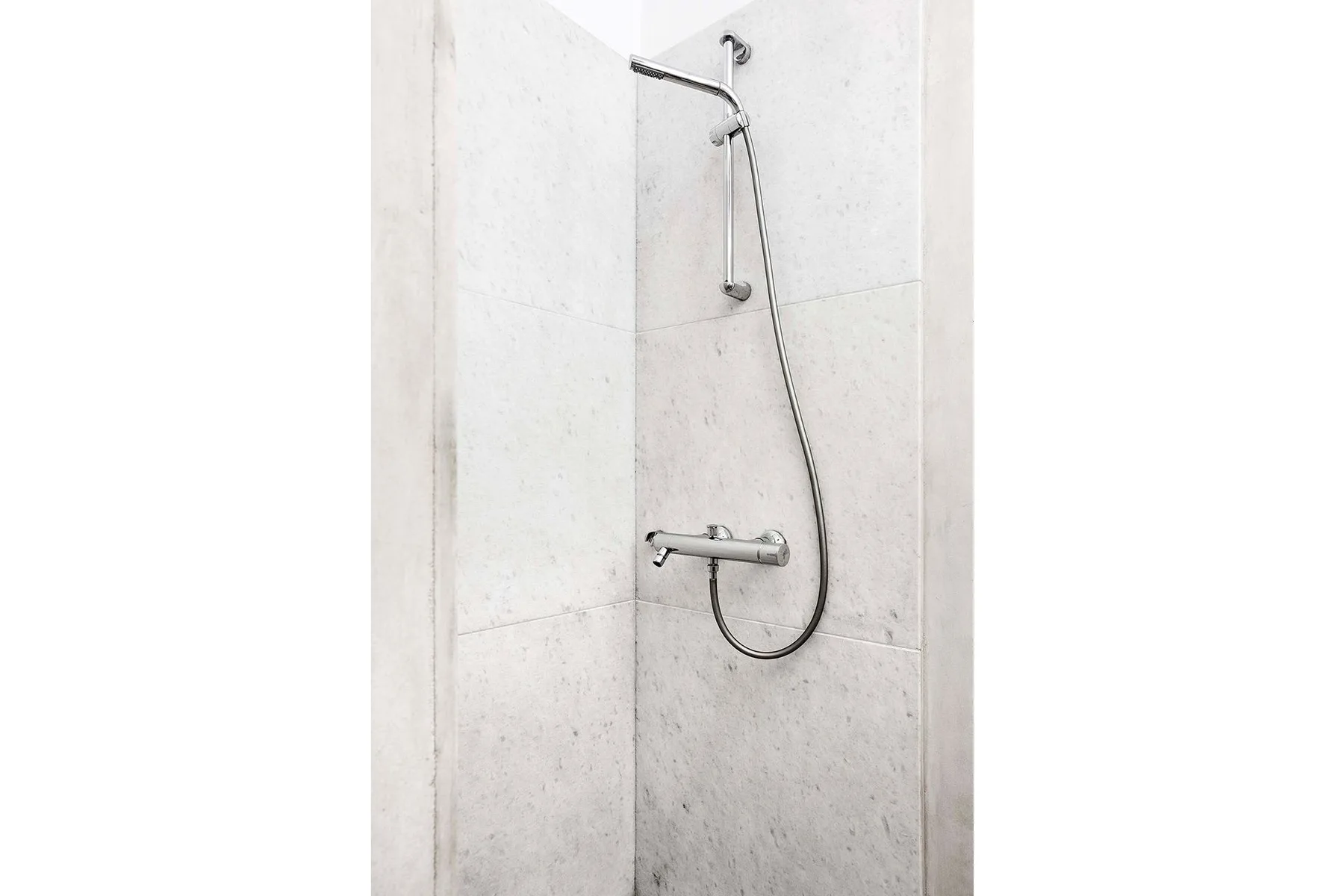 A shower with a handheld showerhead against light tiled walls.