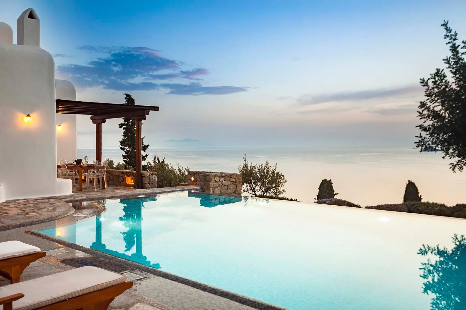 An outdoor swimming pool overlooks a hazy sea beside a white building.