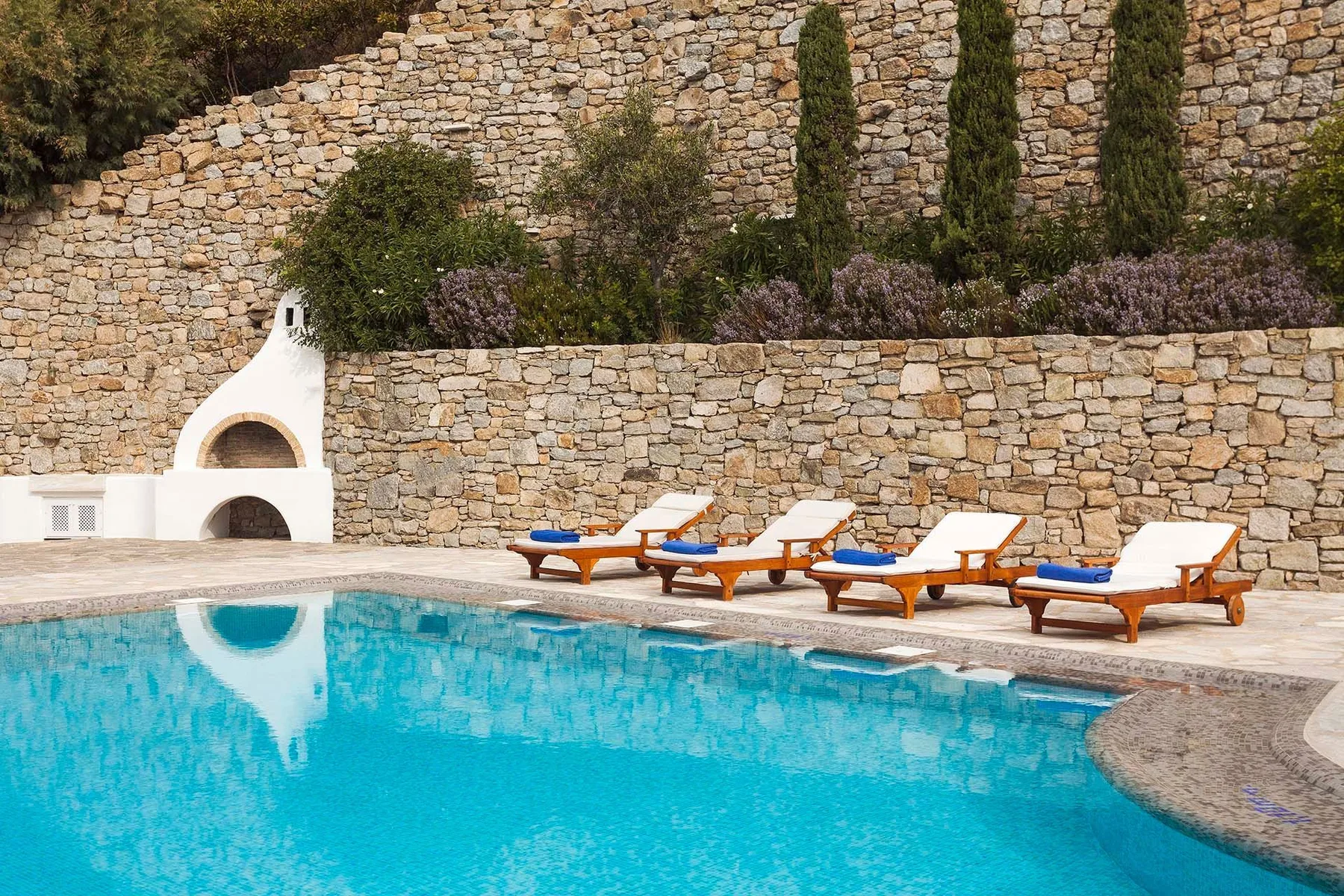 An outdoor swimming pool bordered by lounge seating and stone walls.