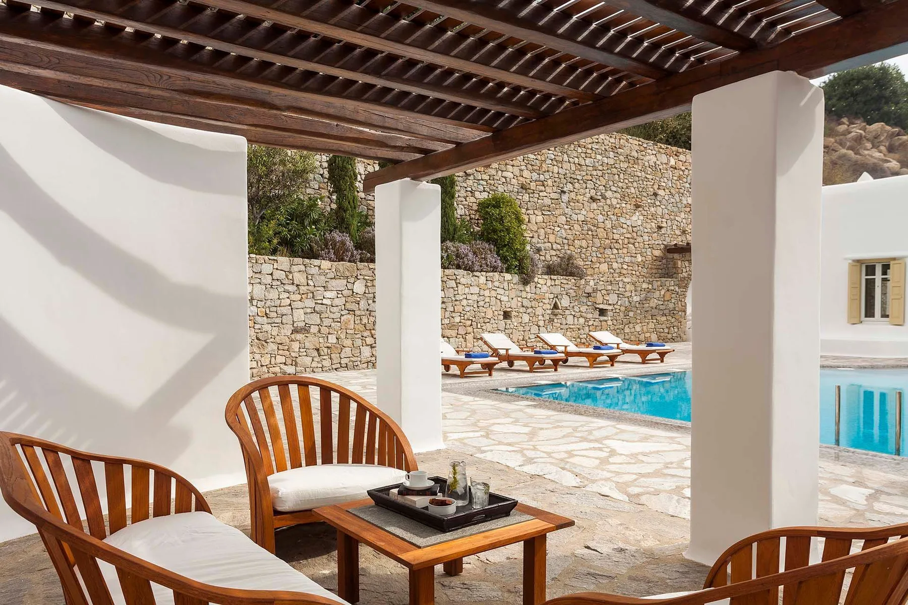 A shaded patio seating area overlooks a swimming pool and stone wall.