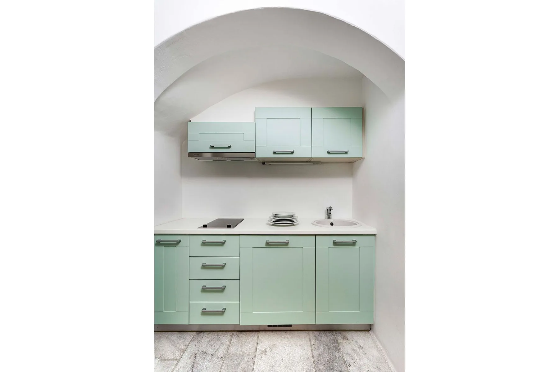 A mint-green kitchen with cabinets, a countertop, and a sink beneath an arched alcove.