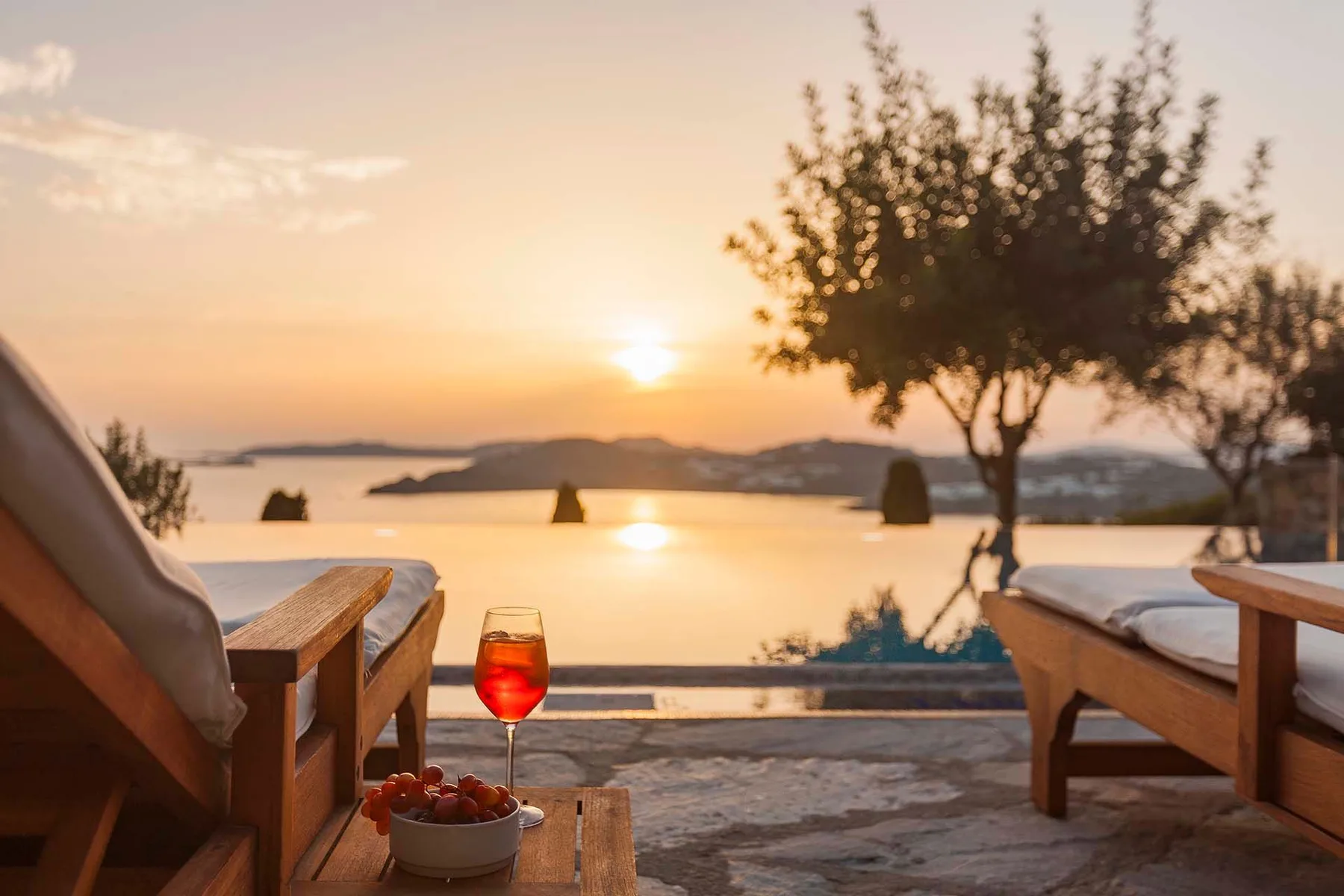 Outdoor seating overlooks the water at sunset, with a small table in the foreground.