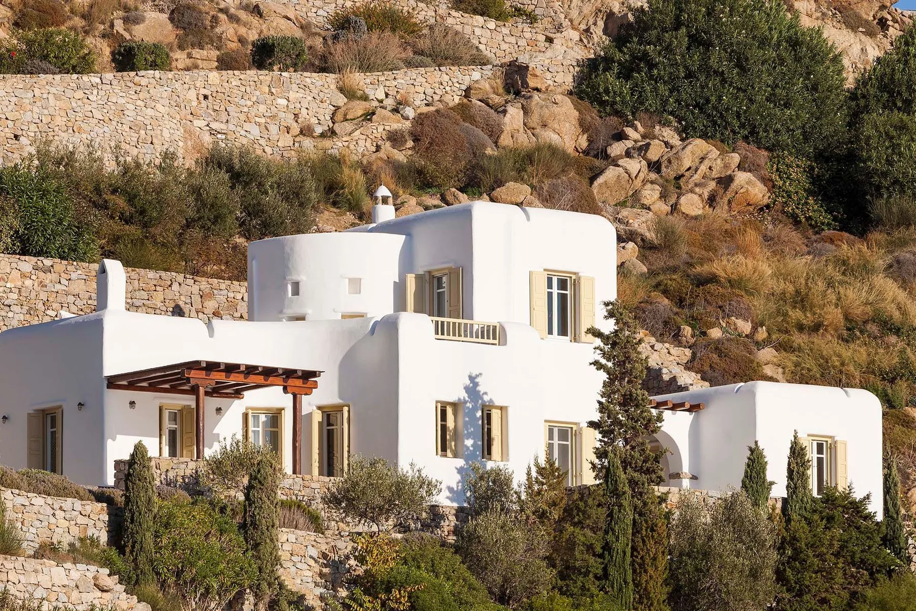 White buildings sit among stone terraces and shrubs on a rocky hillside.