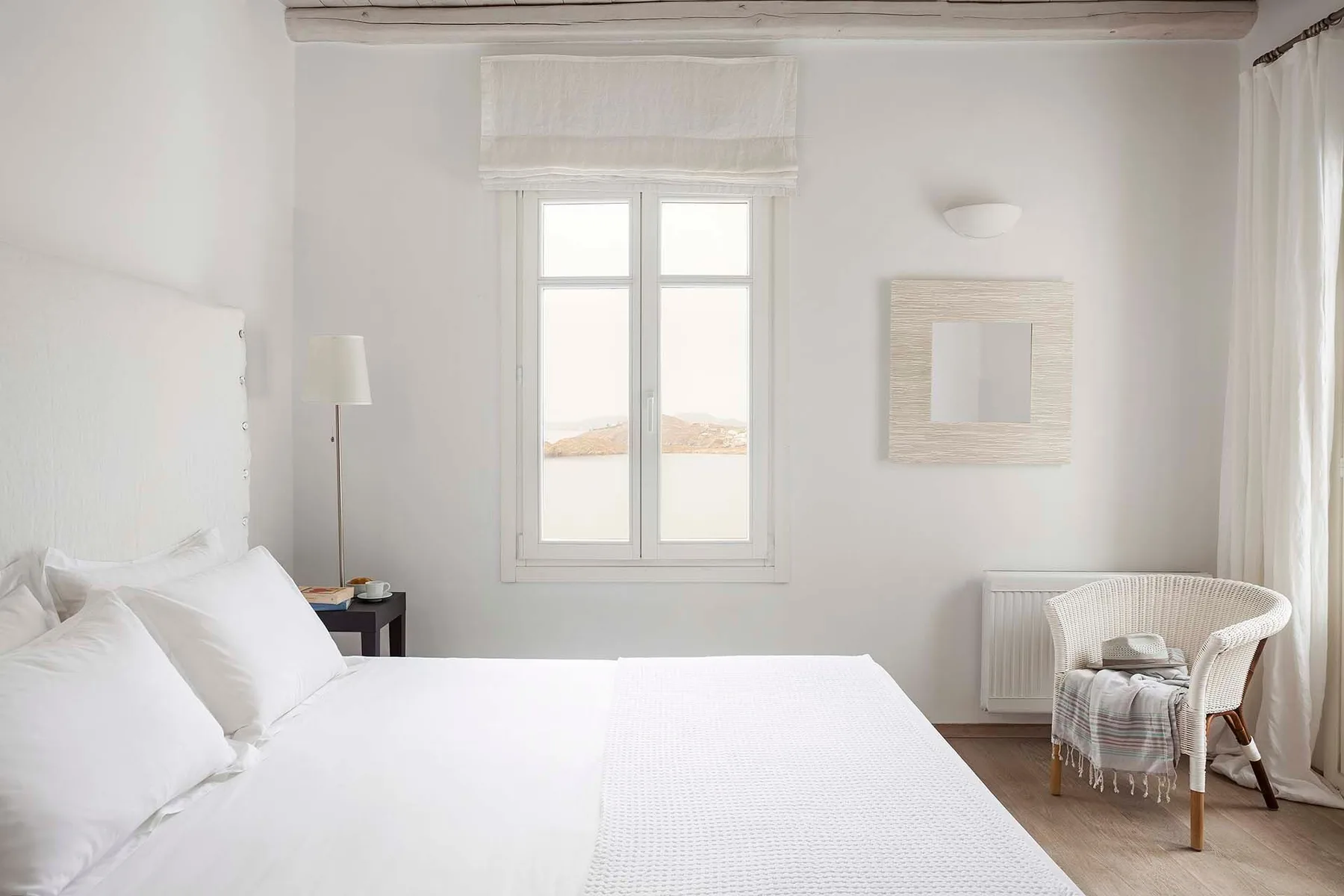 A bright bedroom with a neatly made bed and a window overlooking the landscape.