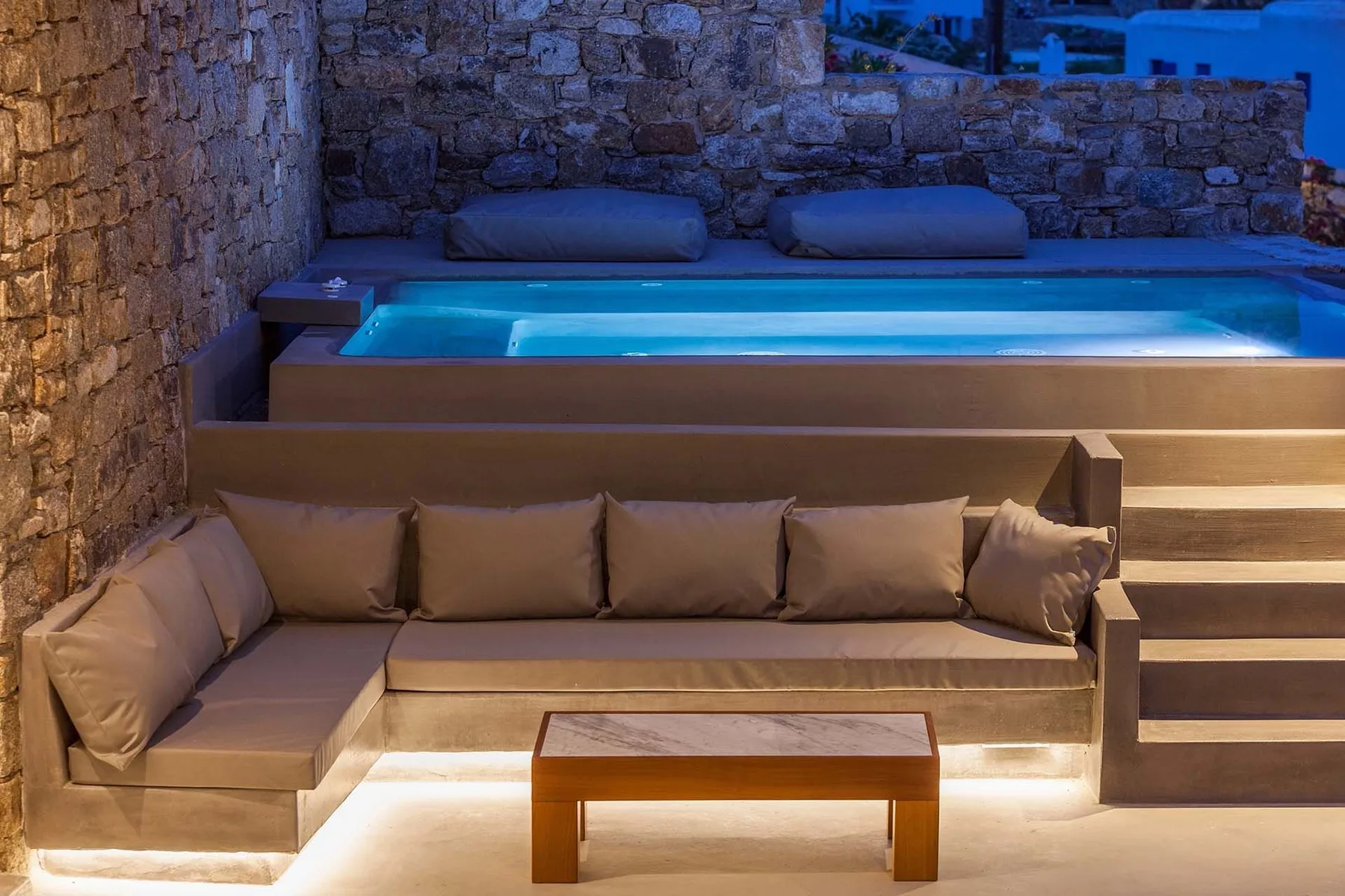 An outdoor lounge with cushioned seating beside an illuminated pool.