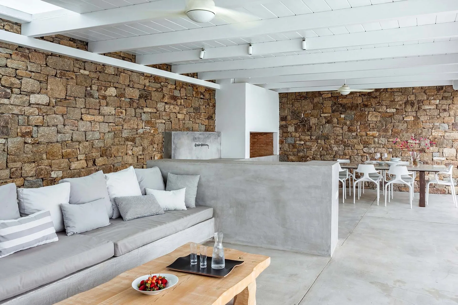 A lounge with gray seating and a dining area against stone walls.