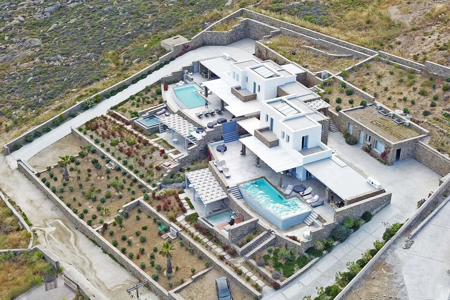 An aerial view of a modern white villa with swimming pools and landscaped grounds.