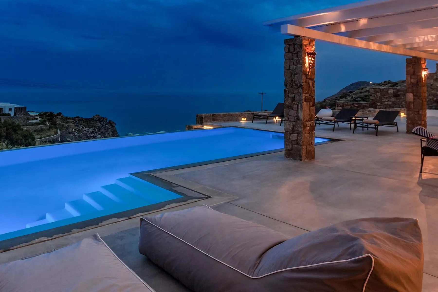 An illuminated swimming pool beside a patio with outdoor seating at dusk.
