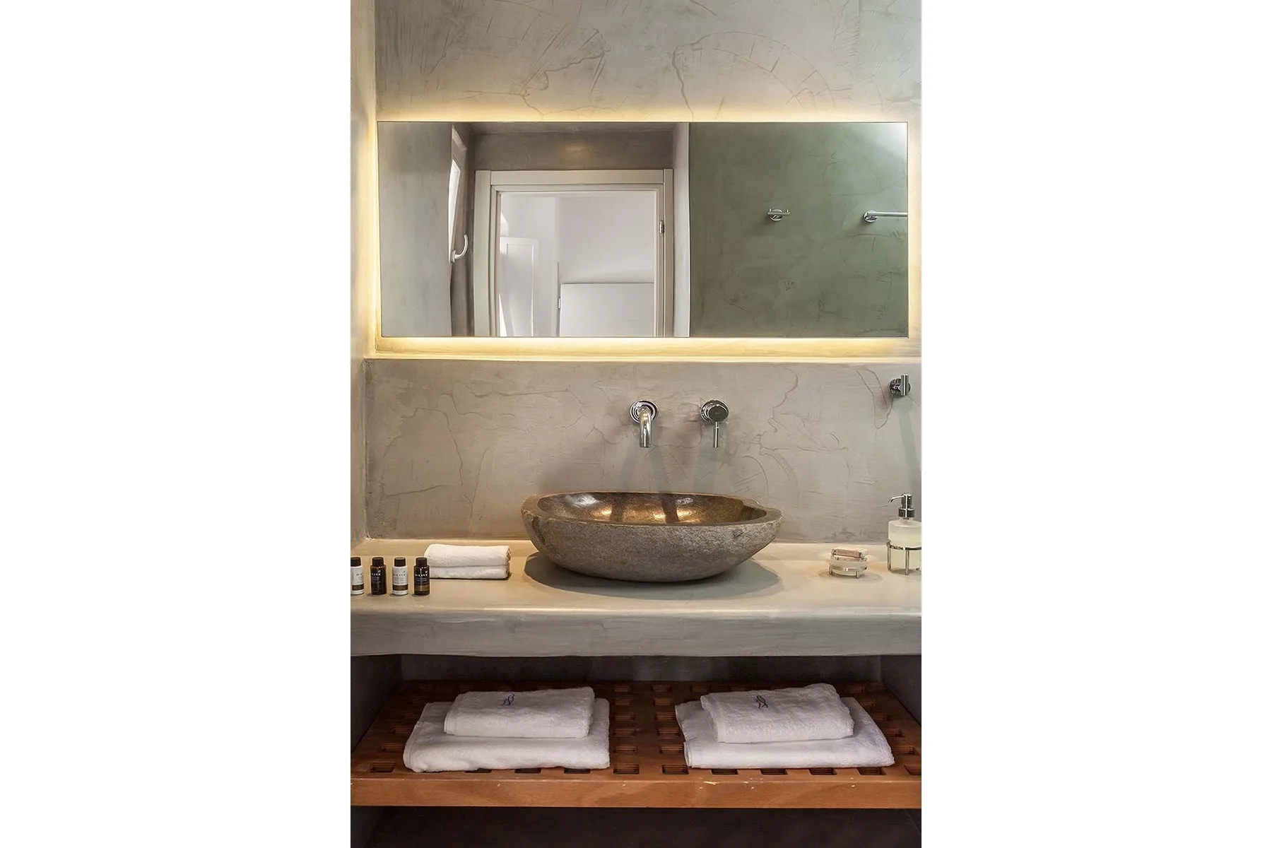 A bathroom vanity with a vessel sink, illuminated mirror, and folded towels on a shelf.