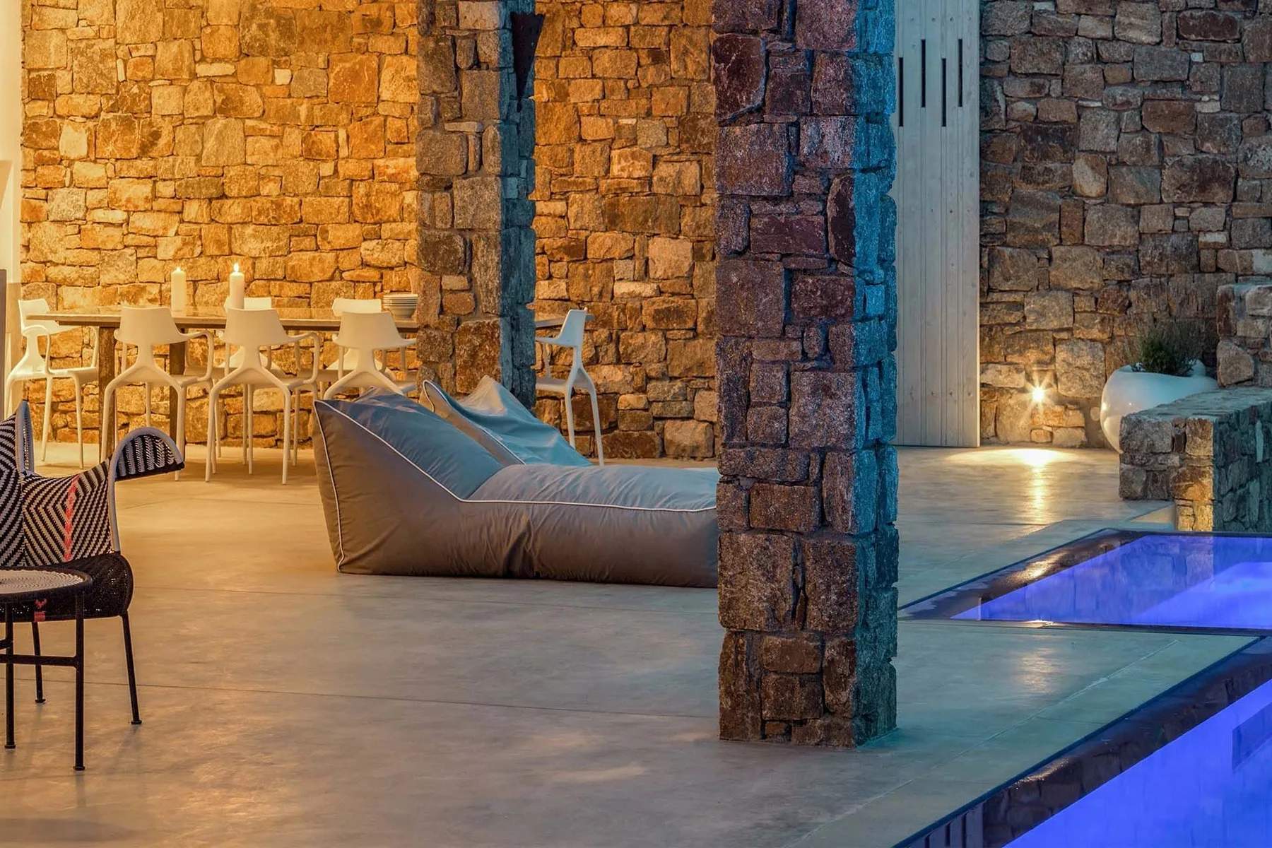 A stone-walled lounge with seating beside a blue-lit pool.
