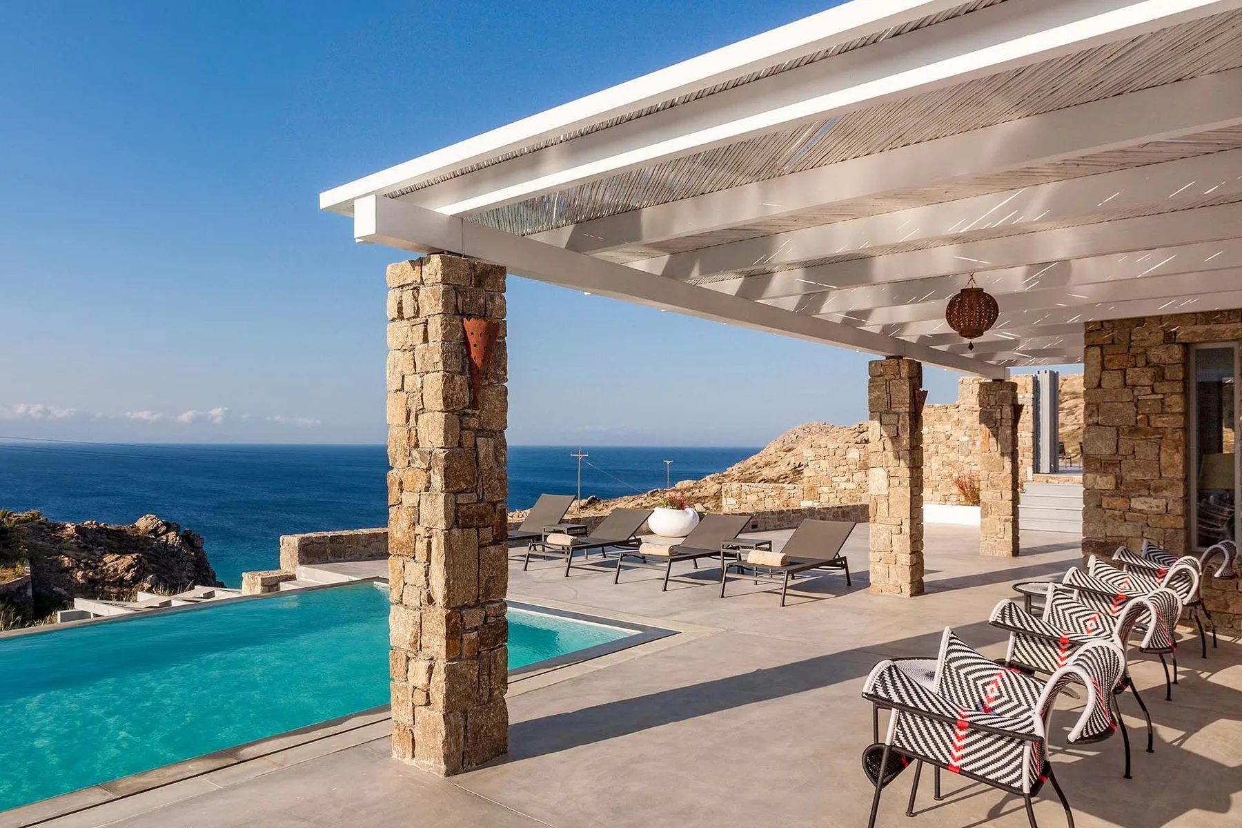 A seaside patio with a swimming pool, lounge seating, and open views of the sea.