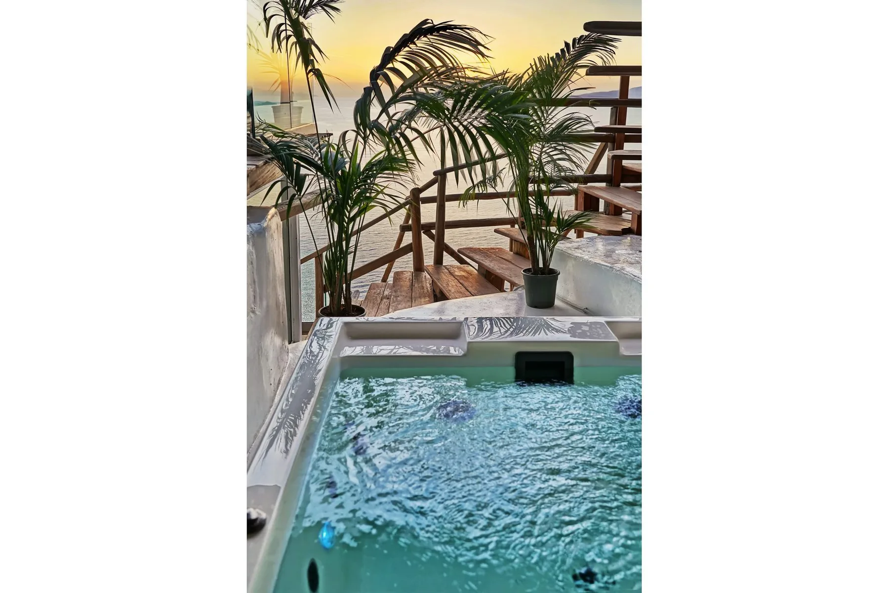 A small outdoor pool sits beside potted palms and a wooden deck at sunset.