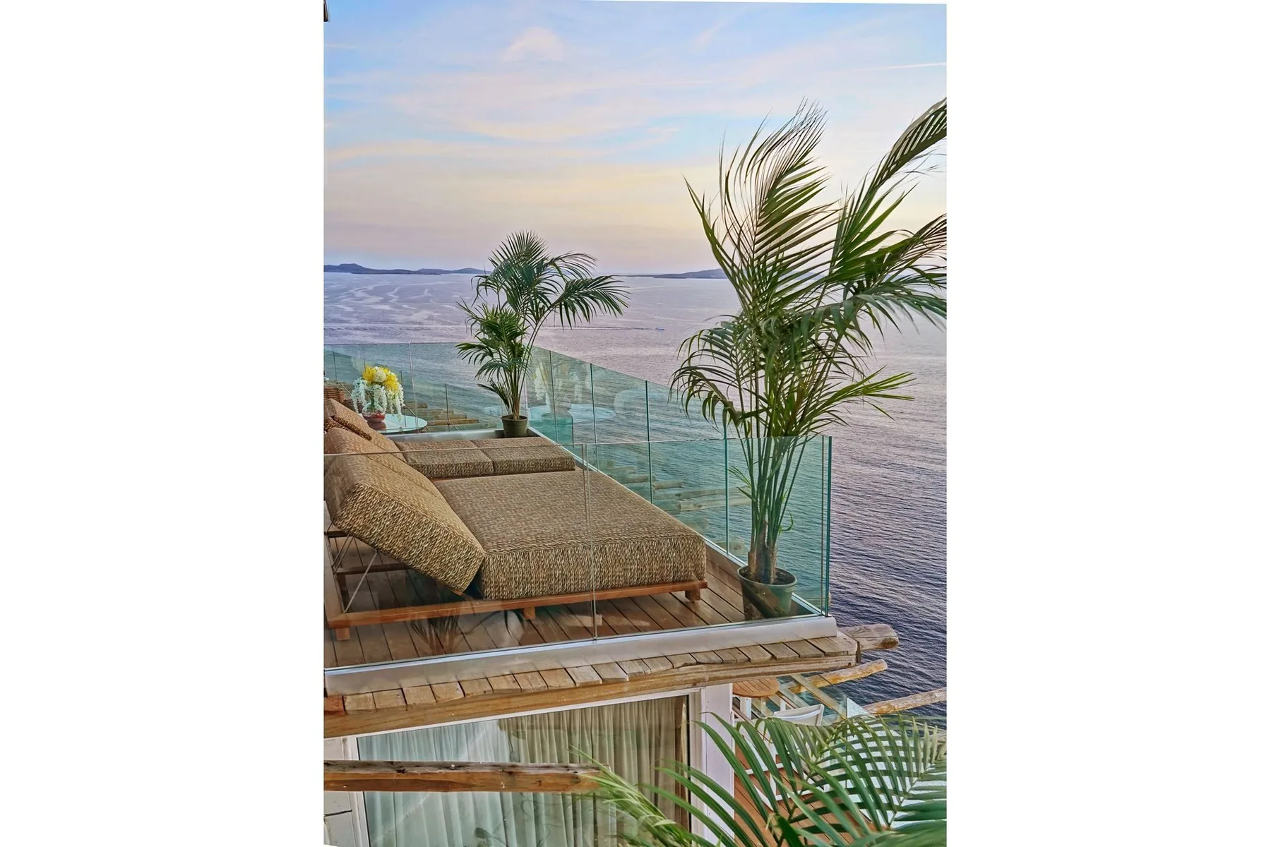 A seaside terrace with lounge seating and palm plants overlooks the water.