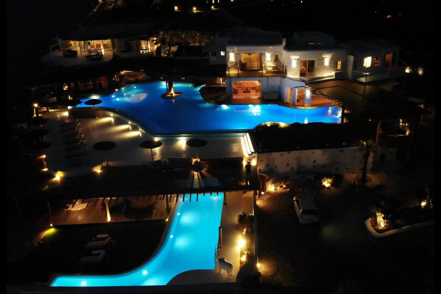 A resort pool glows blue among illuminated buildings at night.