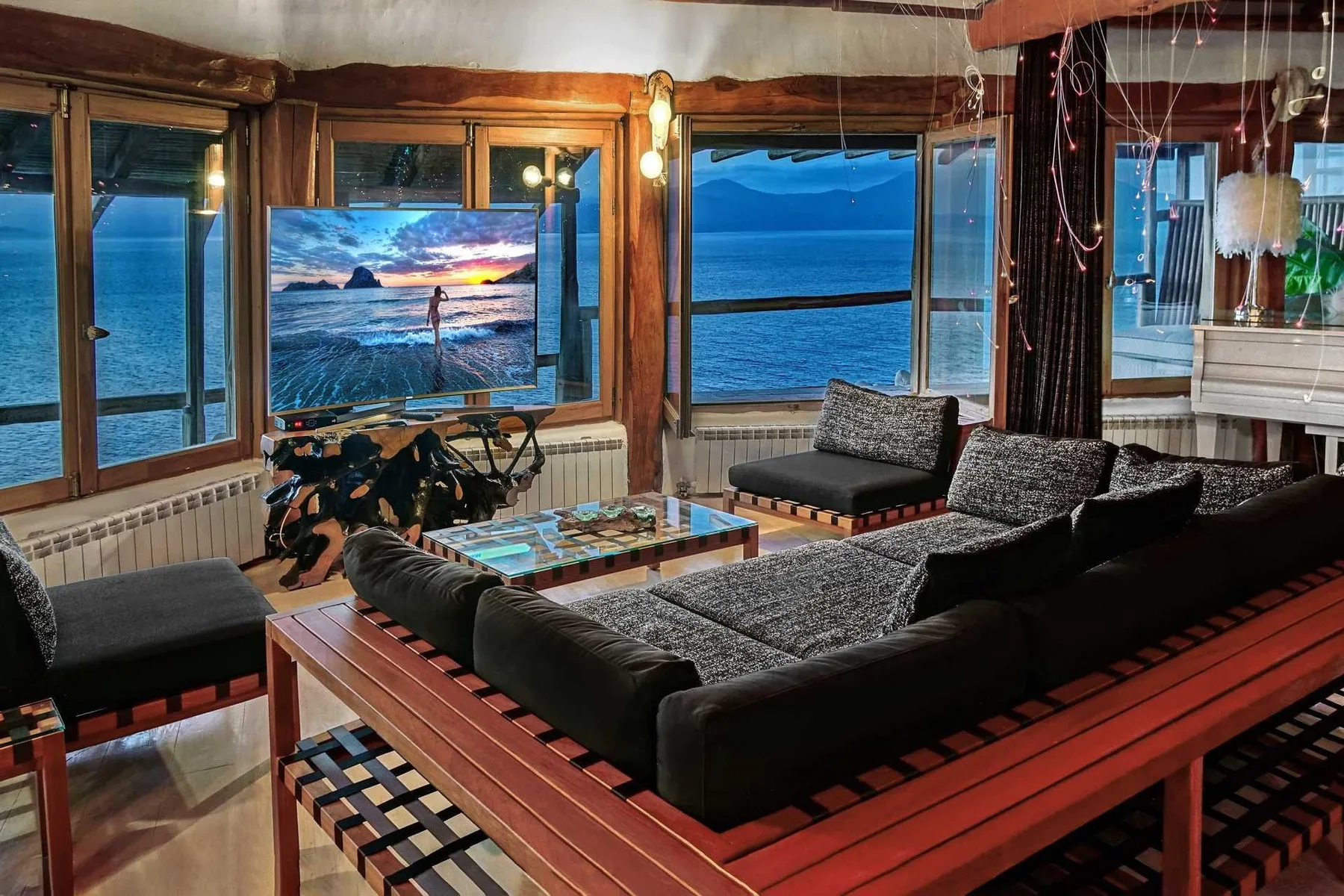A living room with dark seating arranged around a low table beside large windows overlooking the water.