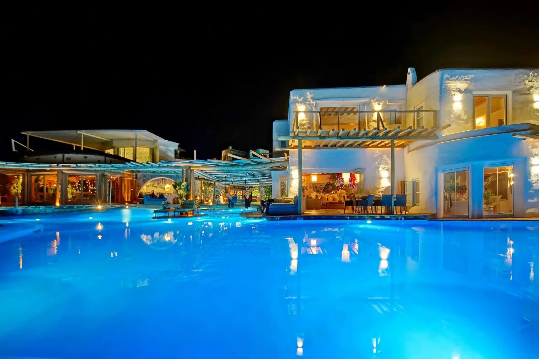 A brightly lit swimming pool sits beside a modern building at night.