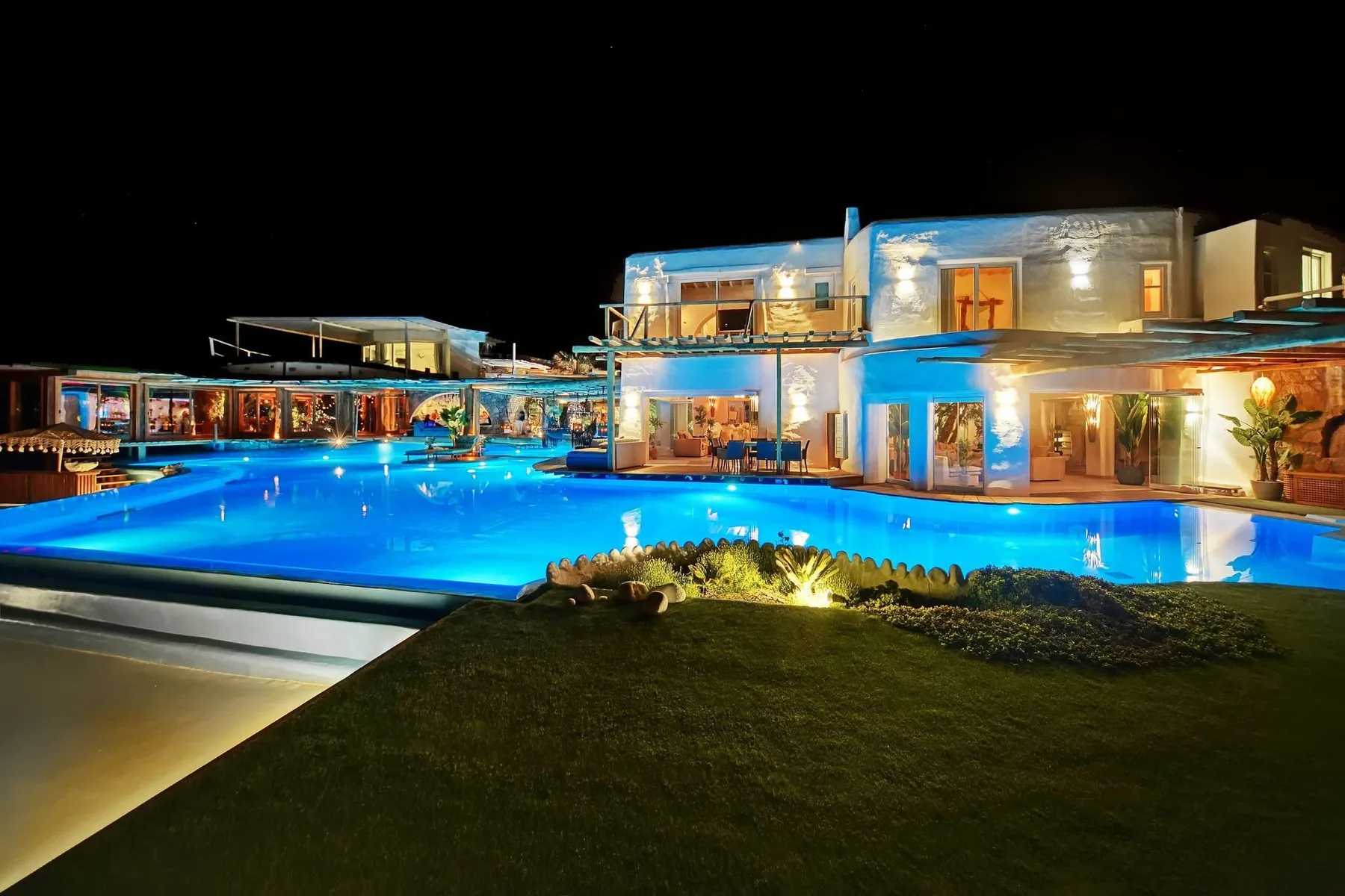 A modern building and illuminated swimming pool are shown at night.