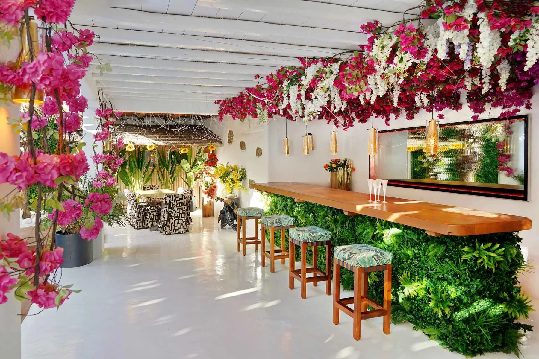 A bright bar area features a long counter, stools, and abundant flowers and greenery.