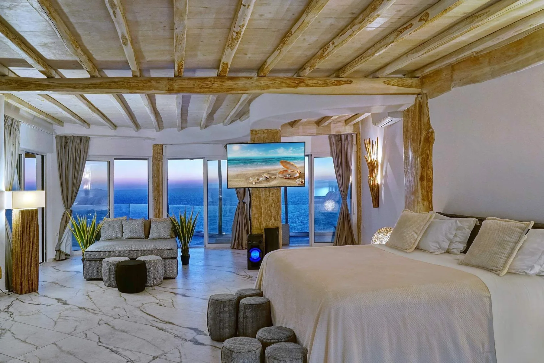 A bedroom with a large bed, lounge seating, and floor-to-ceiling windows overlooking the sea.