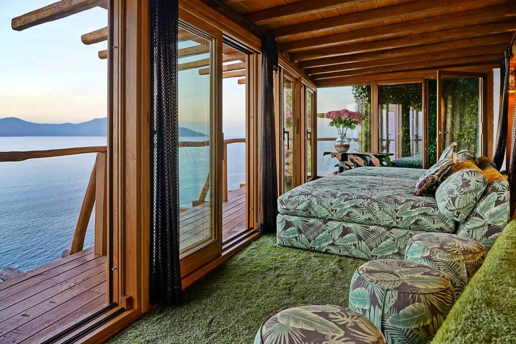 A sunroom with patterned seating beside large windows overlooking the water.