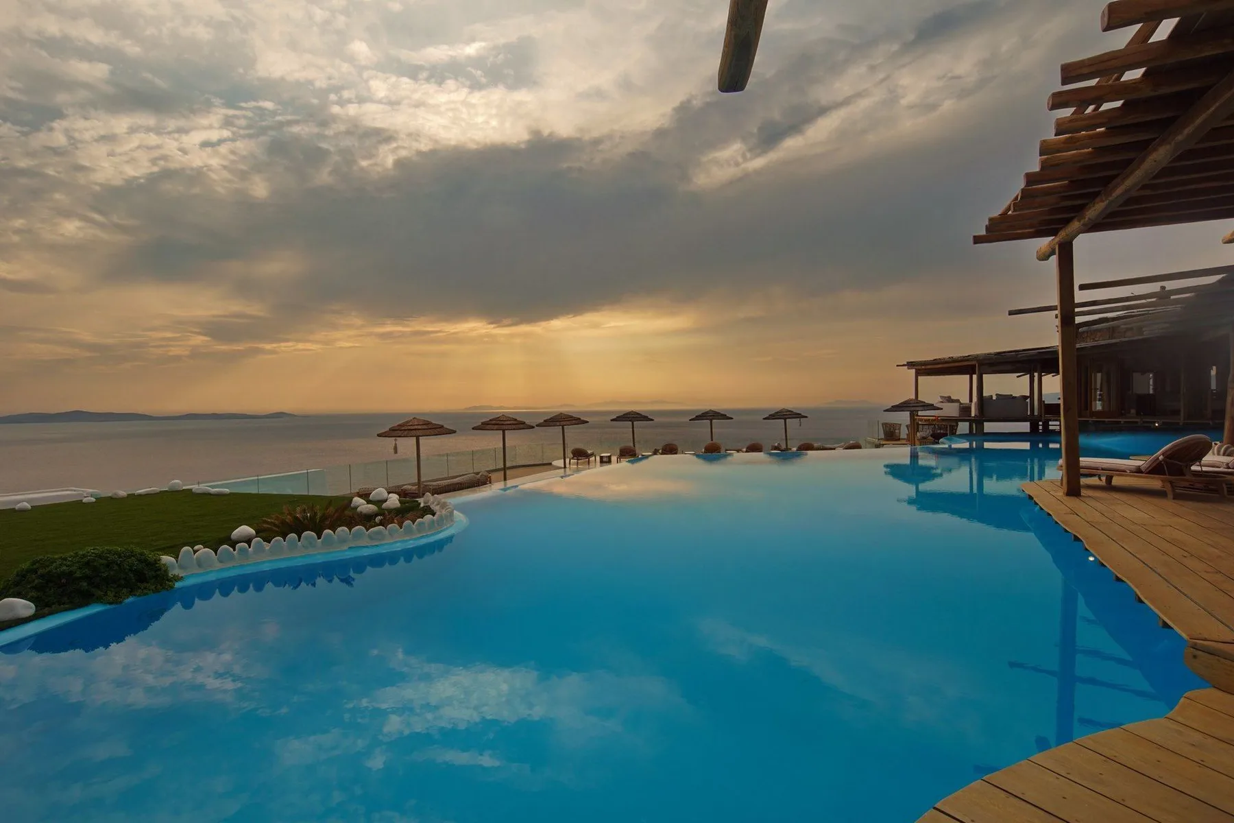 An outdoor pool overlooks the shoreline beneath a cloudy sunset sky.