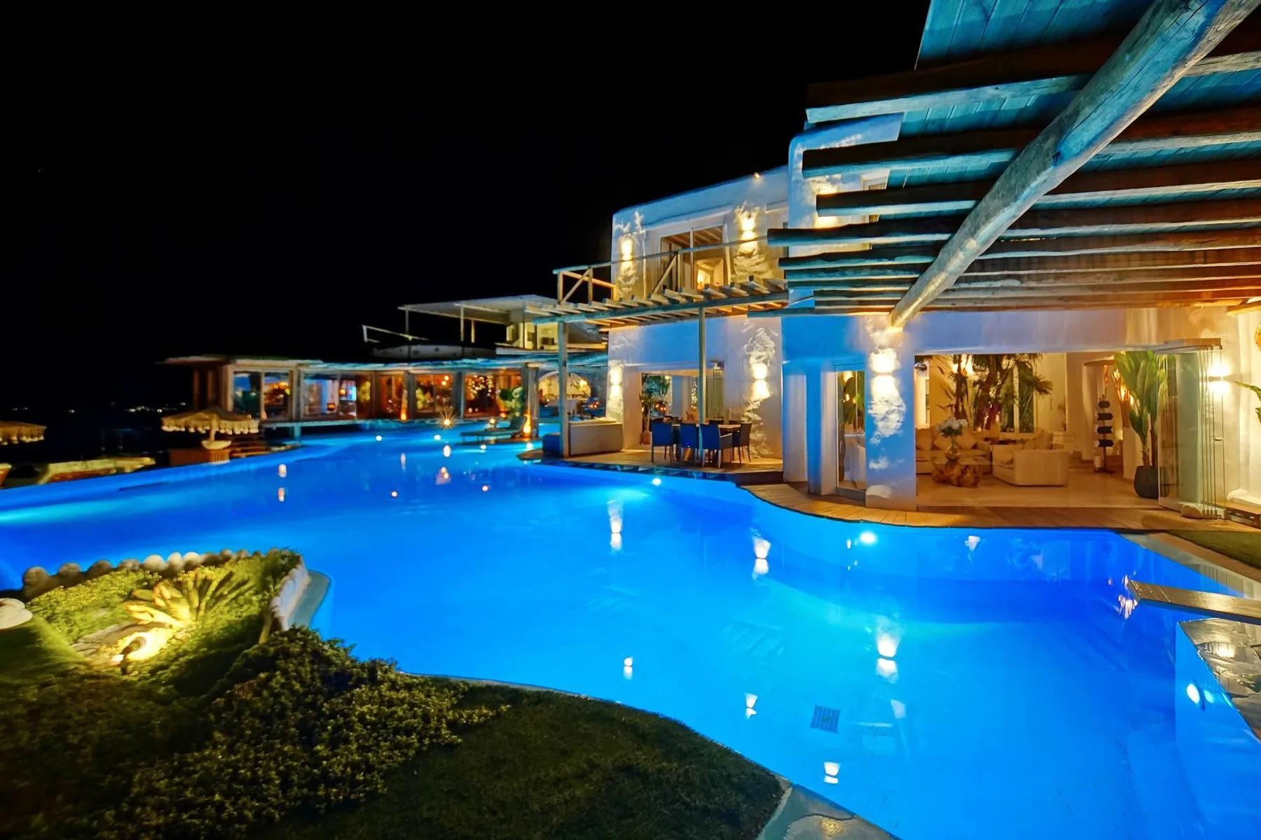 A brightly lit swimming pool at night beside a modern building.