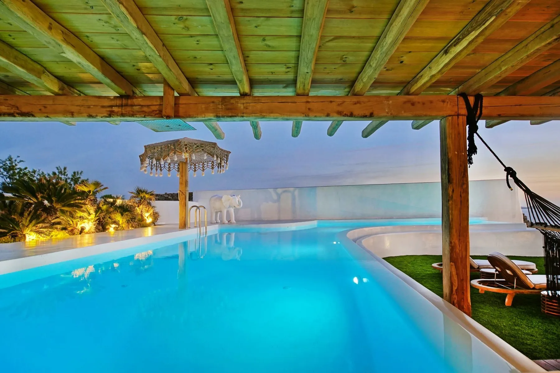 A swimming pool beneath a wooden pergola, with lounge seating beside the water.