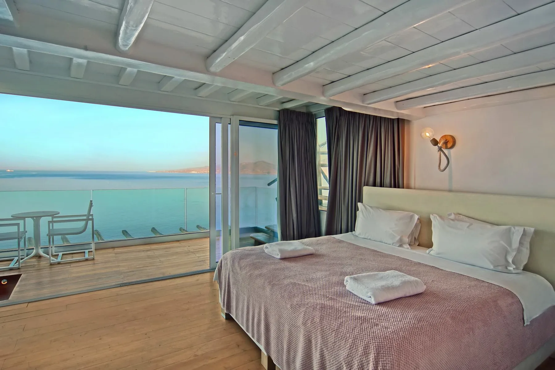 A bedroom with a bed beside glass doors opening onto a balcony with a sea view.