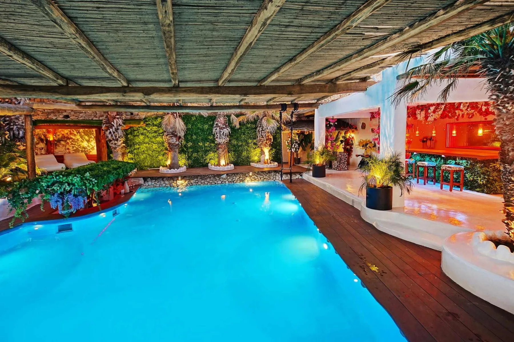 A swimming pool sits beneath a timber canopy beside a wooden deck.