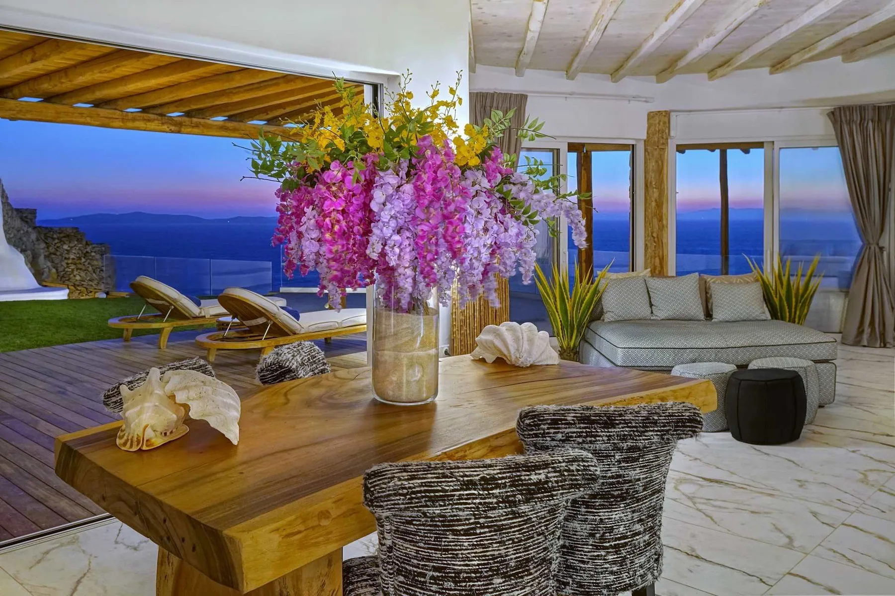 A bright living room opens onto a terrace with ocean views and a flower centerpiece.