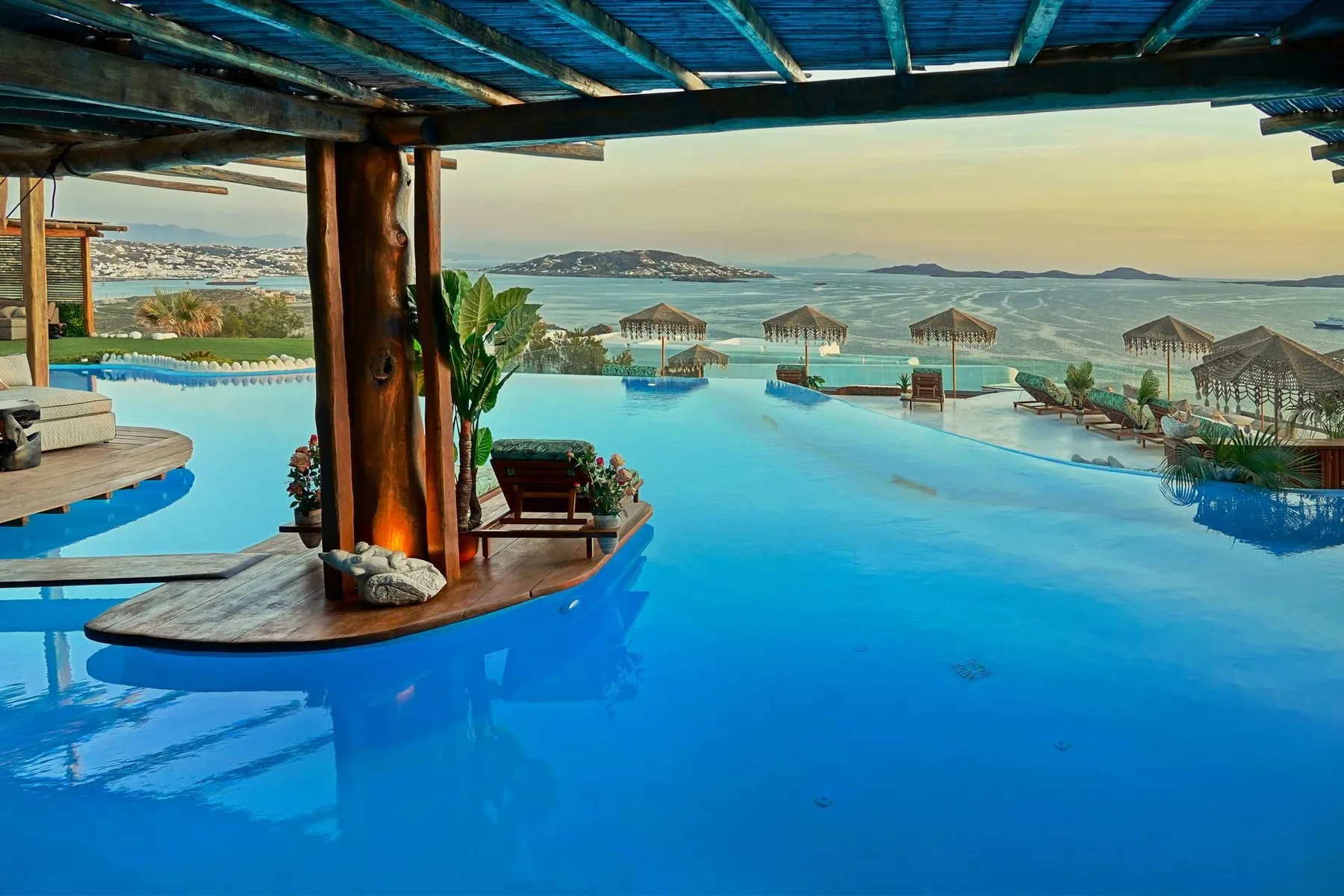 A blue swimming pool overlooks the sea, with shaded seating along the water.