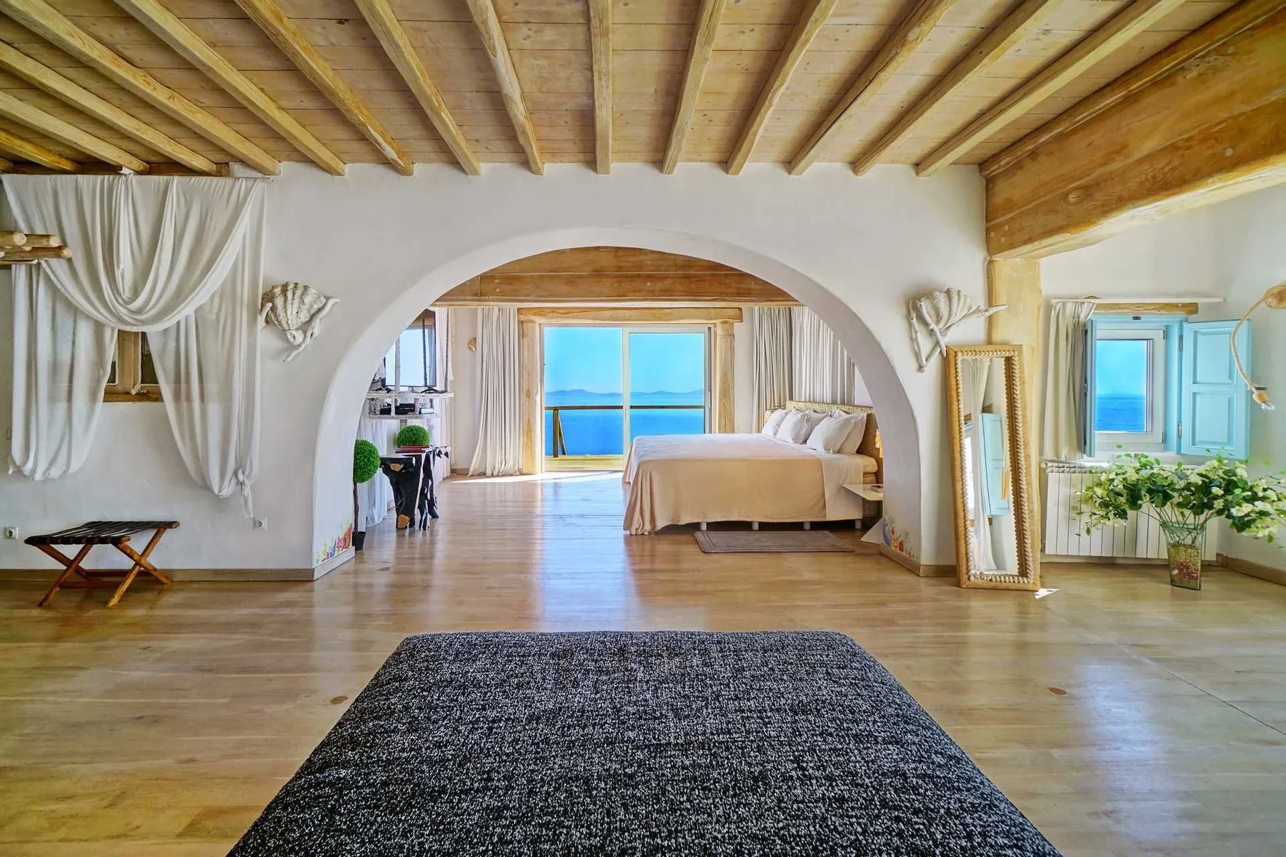 A bright bedroom opens through an arch to a bed beside a large window.