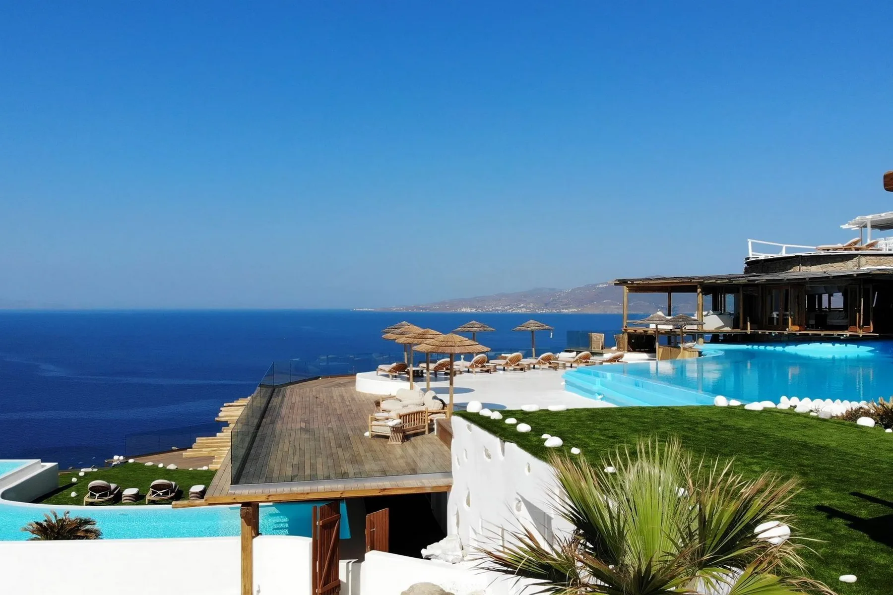 A seaside pool terrace overlooks the blue sea beneath a clear sky.